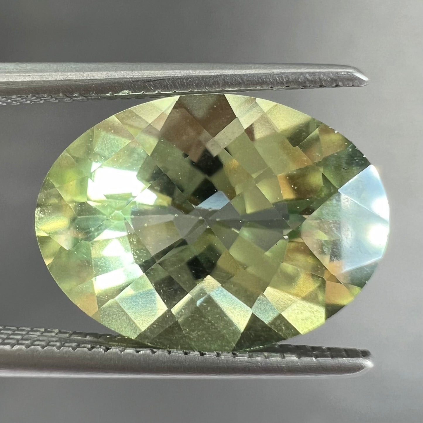 An oval checkerboard cut kiwi mystic topaz gemstone. The stone is a light yellowish green color.
