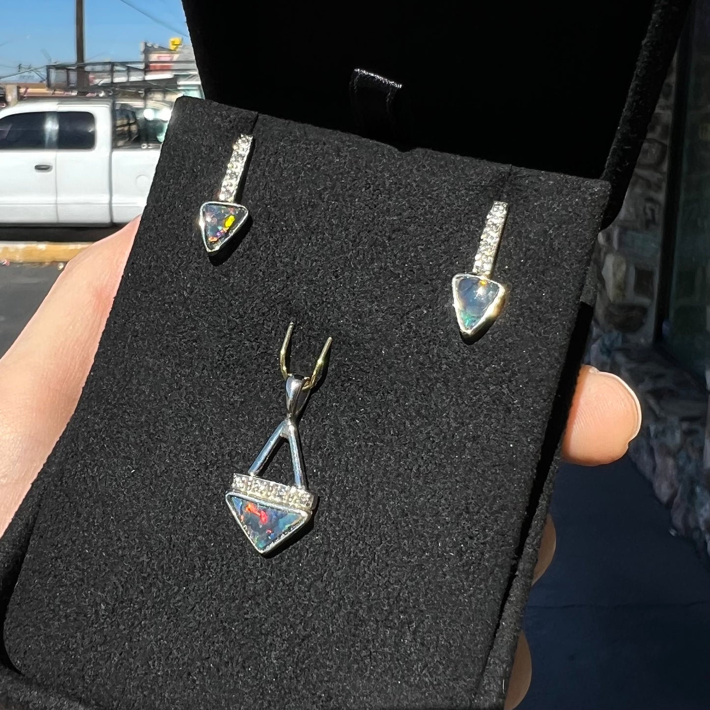 A white gold pendant and earrings set mounted with triangle cut natural black opals and diamonds.