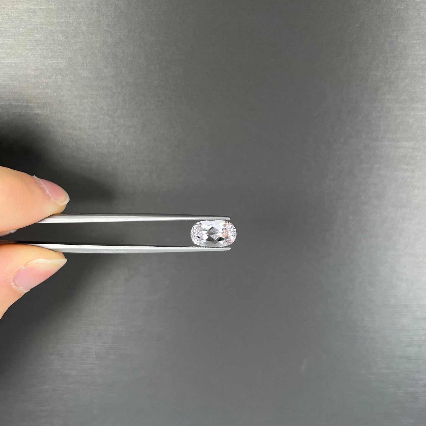A loose, faceted oval cut kunzite gemstone. The stone is a light pink color.