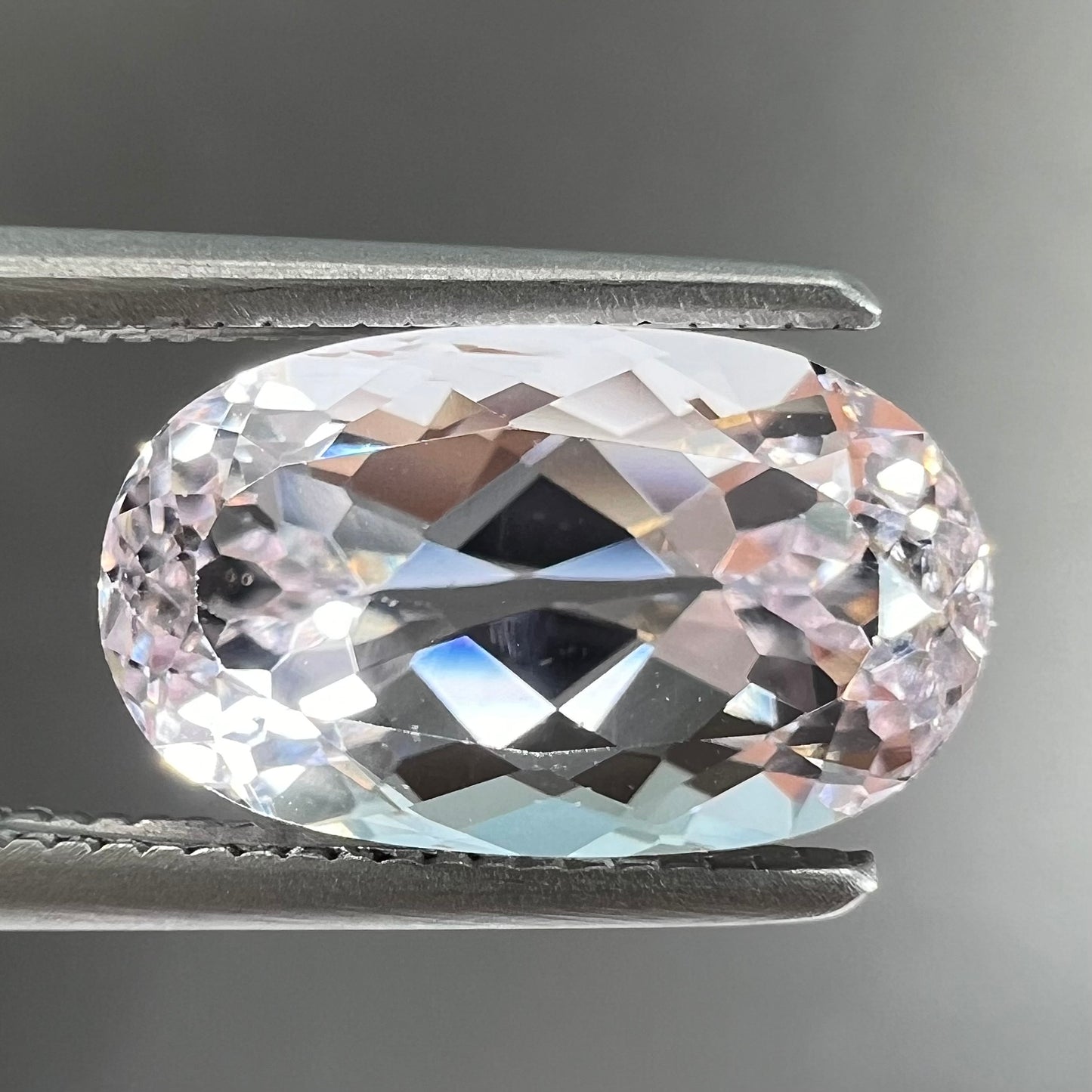 A loose, faceted oval cut kunzite gemstone. The stone is a light pink color.