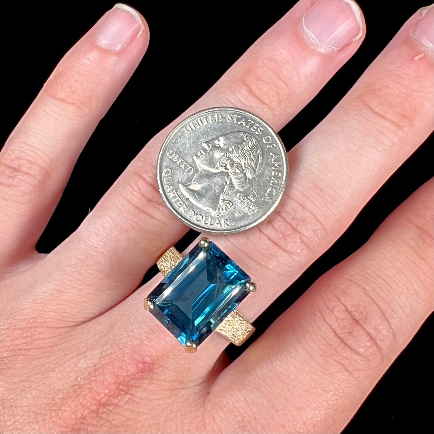 A ladies' yellow gold London blue topaz solitaire ring. The ring is textured, and the topaz is emerald cut.