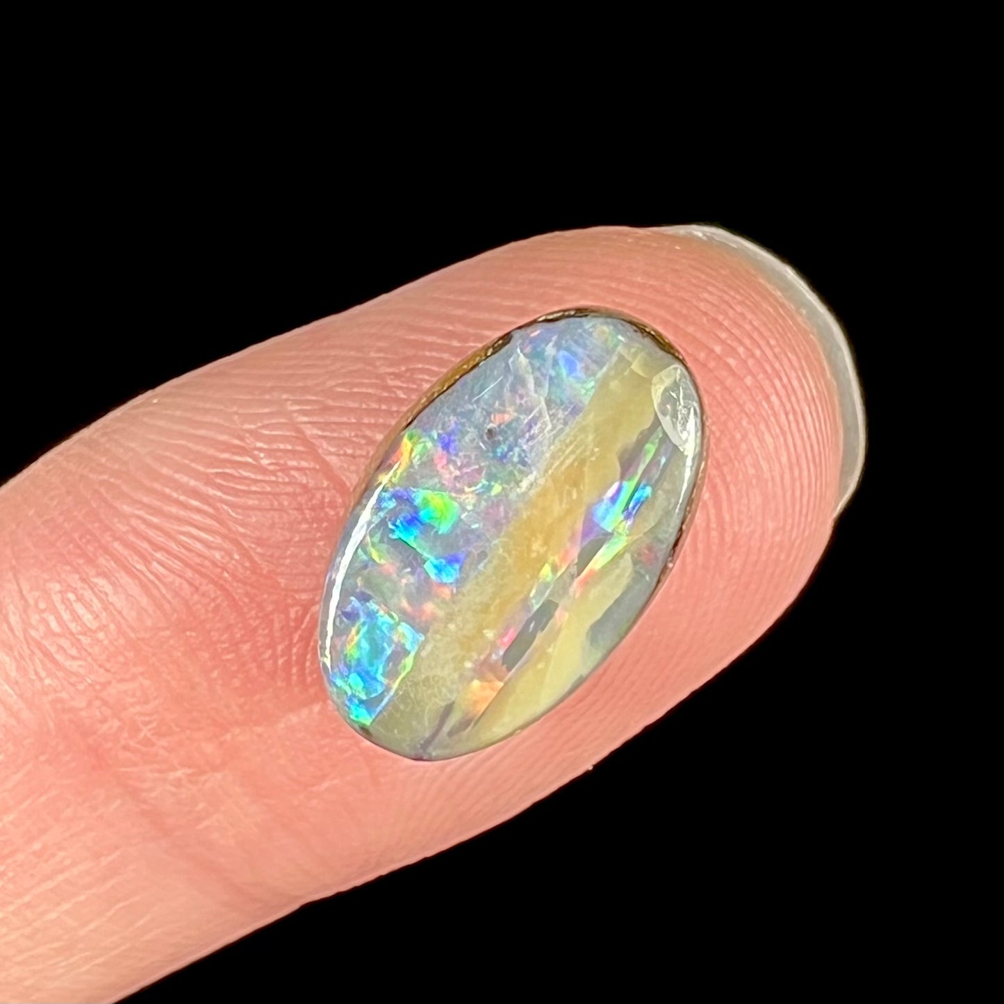 An oval cabochon cut boulder opal from Quilpie, Australia. The opal has multicolor color play.