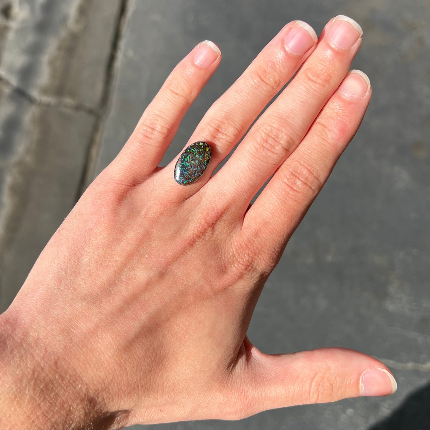A loose, oval cabochon cut Koroit boulder opal stone. The opal has green and blue veins.