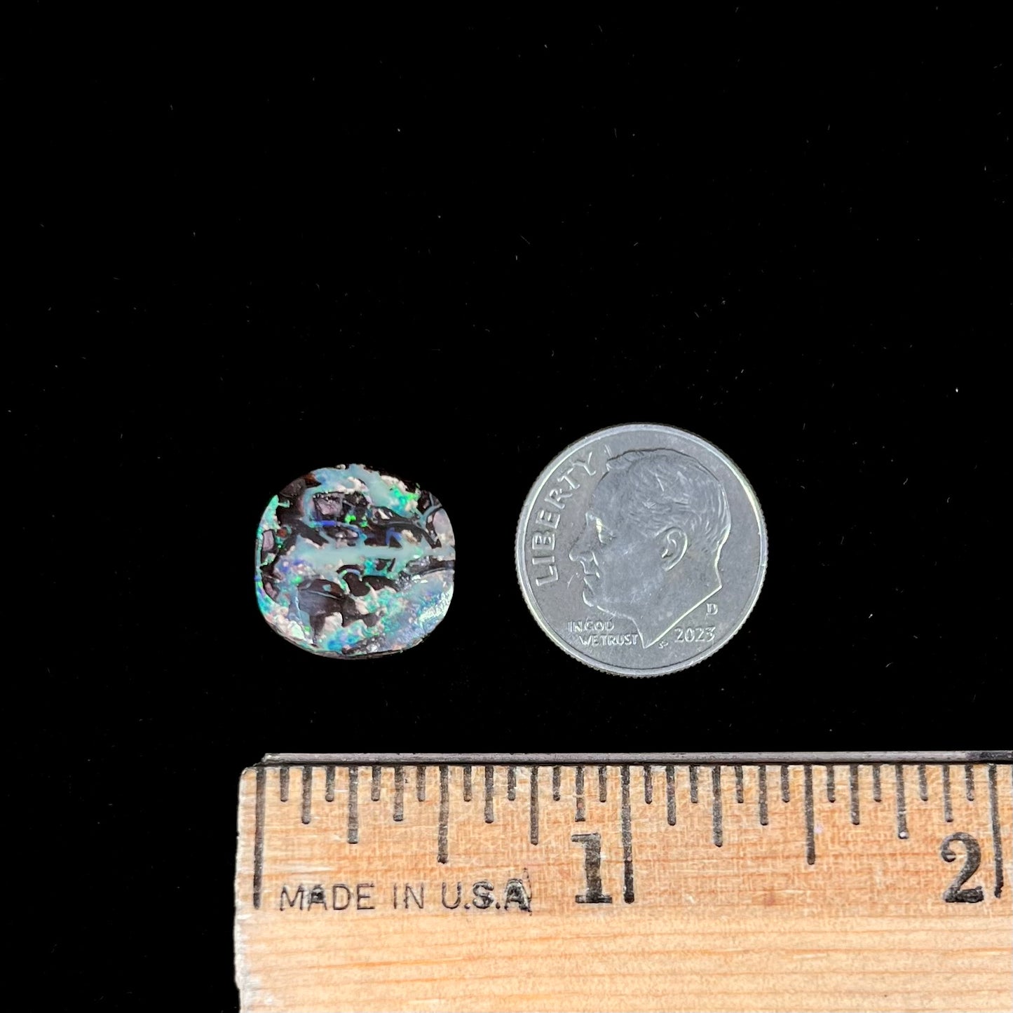 An off-round cabochon cut boulder opal stone from Koroit, Australia. The opal has green, blue, and red colors.