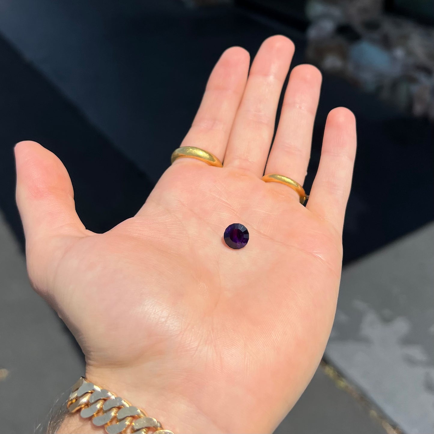 A modified round cut amethyst gemstone. The stone is a dark bluish purple color.
