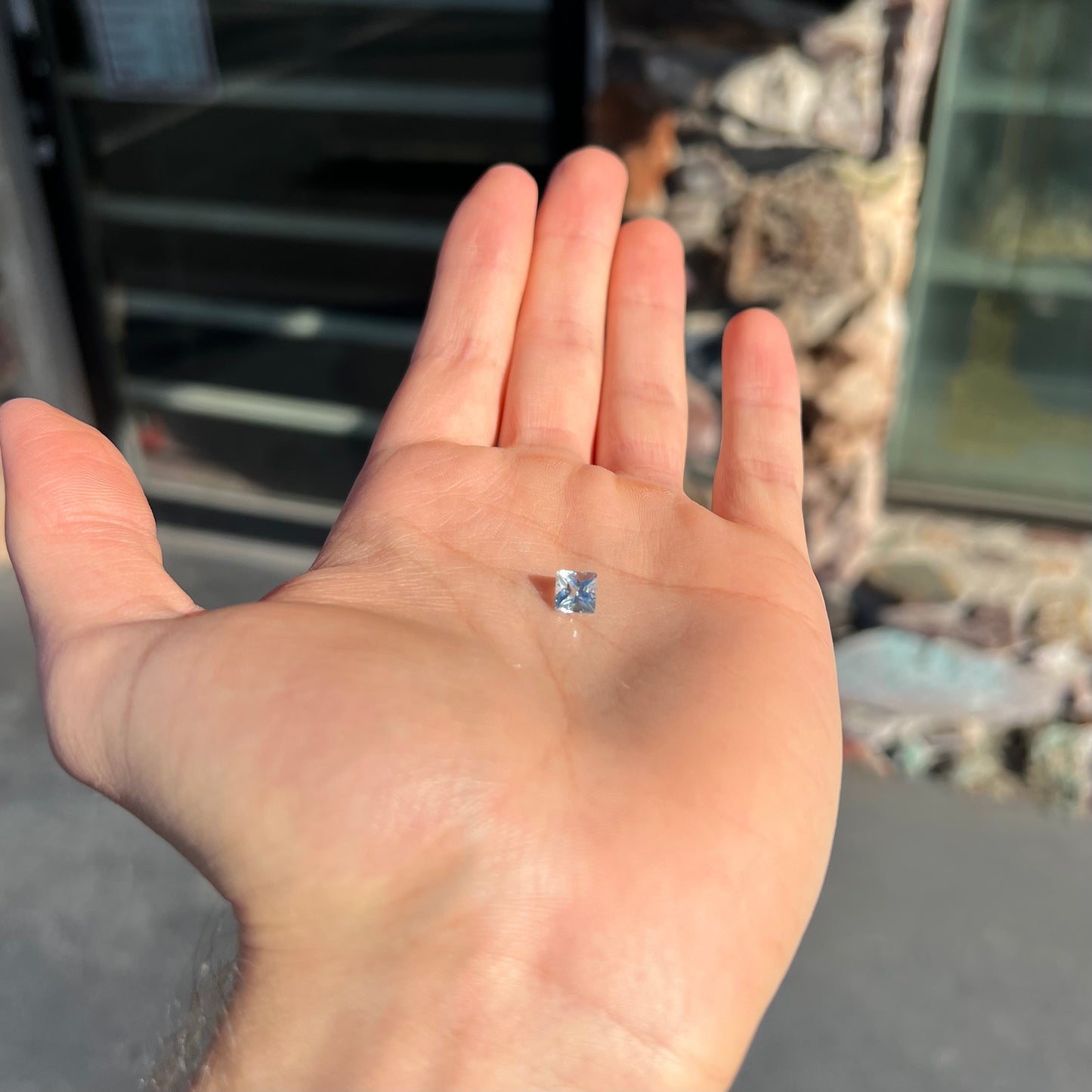 A loose, princess cut aquamarine gemstone. The stone is a light blue color.