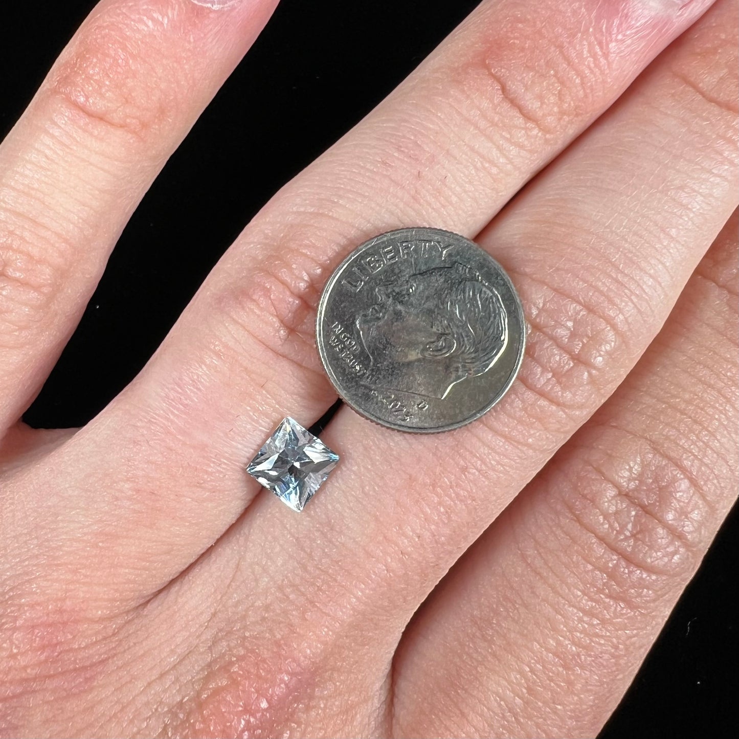 A loose, princess cut aquamarine gemstone. The stone is a light blue color.