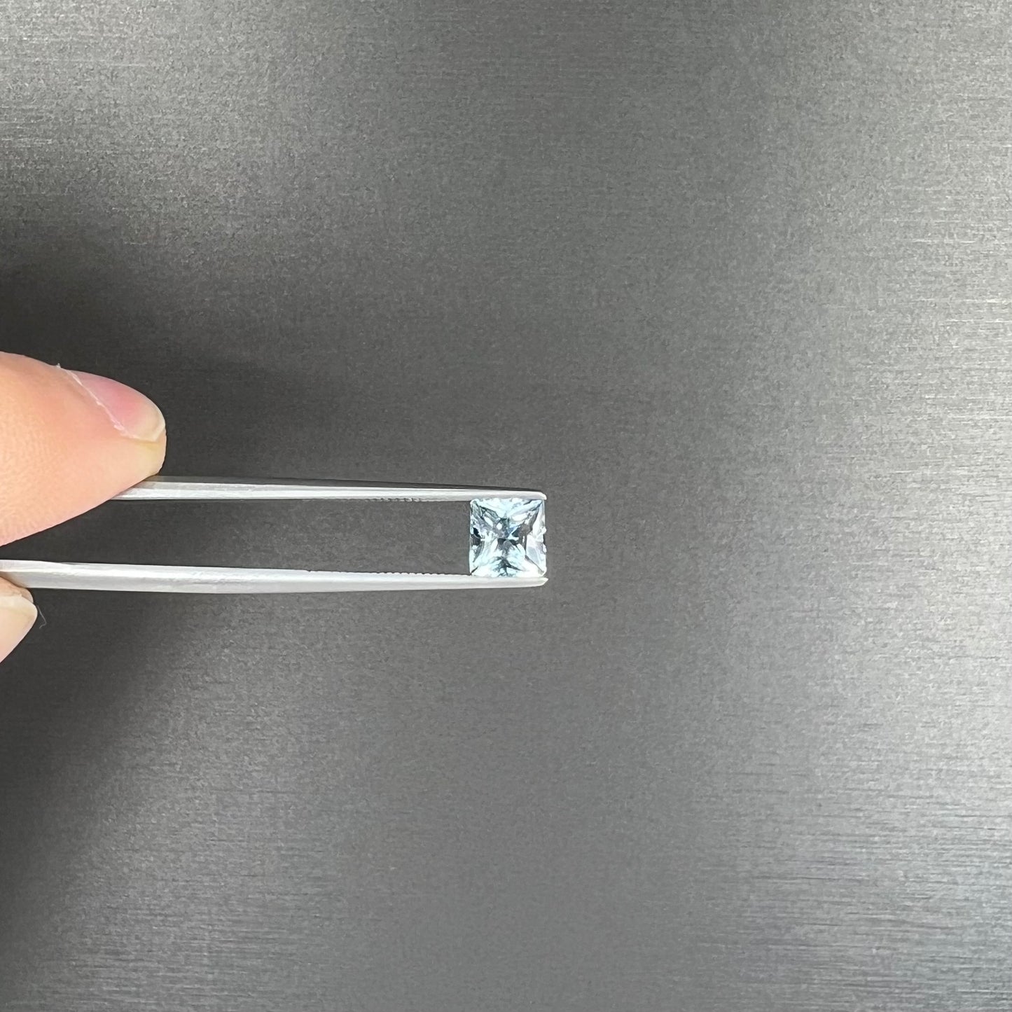 A loose, princess cut aquamarine gemstone. The stone is a light blue color.
