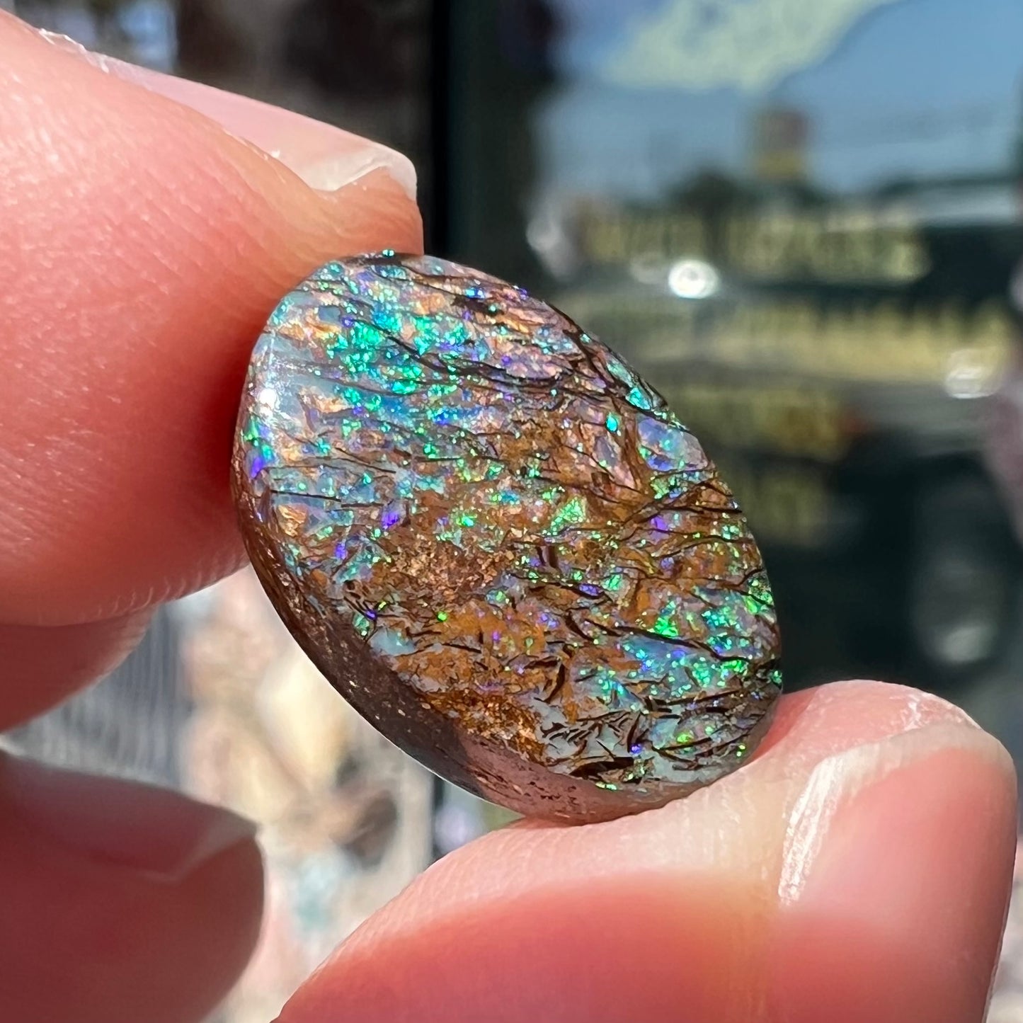 A loose, oval cabochon cut matrix boulder opal stone from Koroit, Australia. The opal shines with green and blue colors.