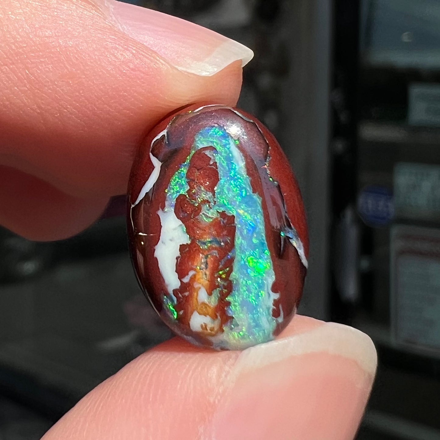 A loose, oval cabochon cut boulder opal stone from Australia. The opal has blue and green veins in an ironstone matrix.