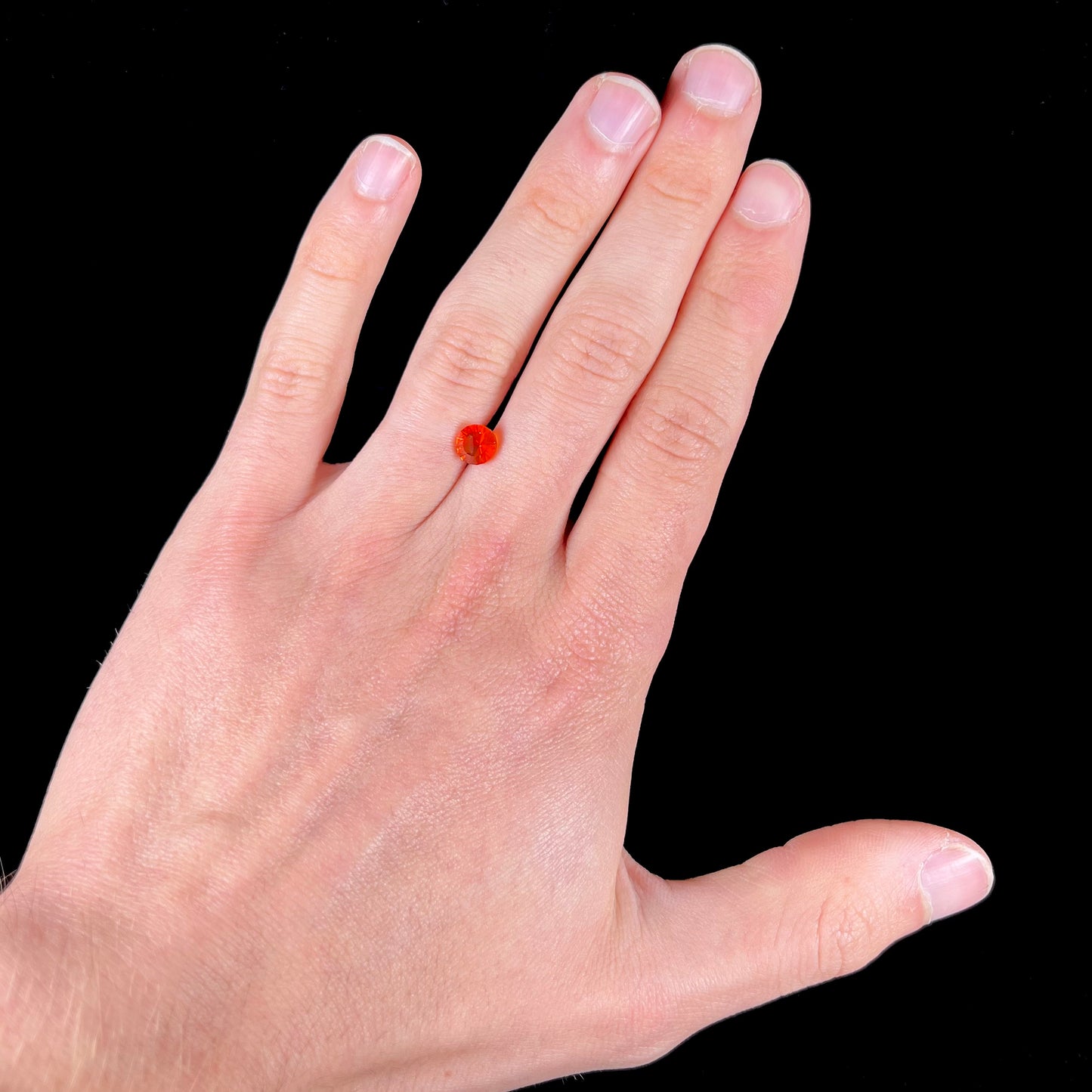 A faceted round cut natural Mexican fire opal stone. The stone is bright orange in color.