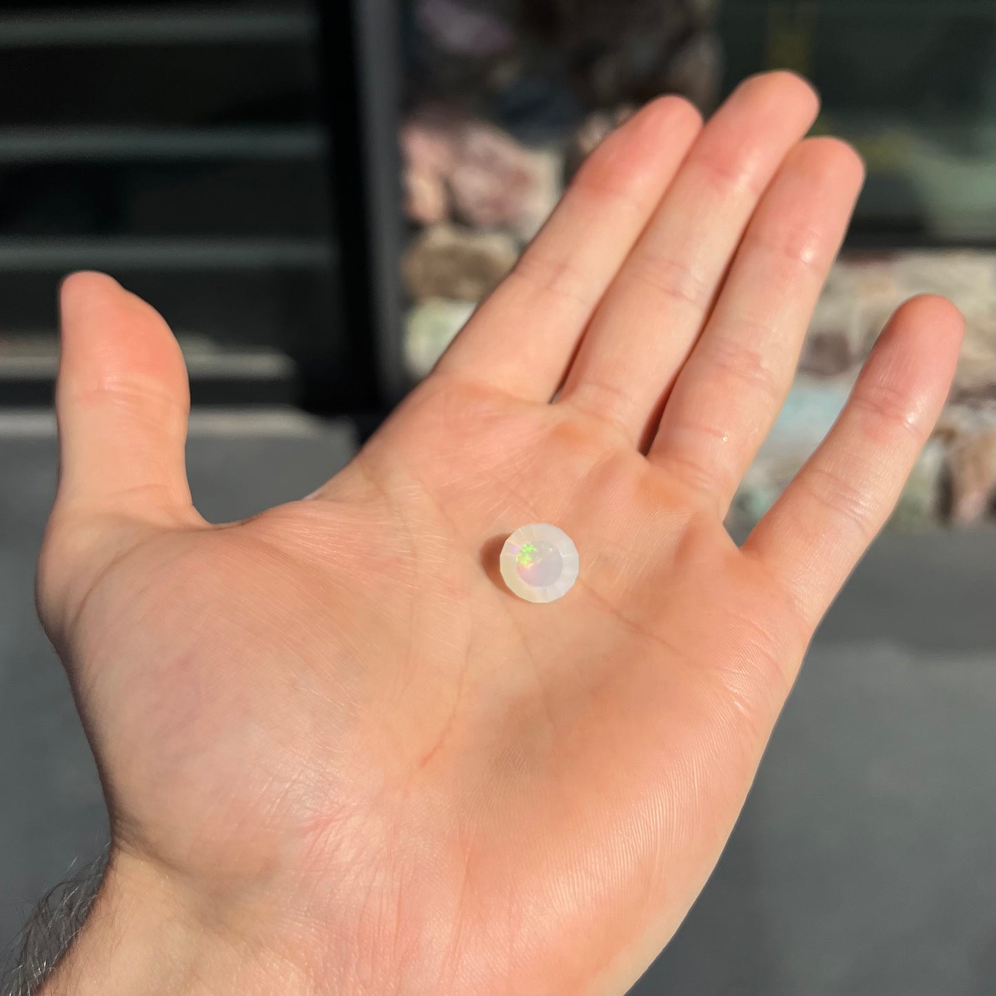 A loose, modified round cut Mexican fire opal gemstone. The stone is transluscent light yellow with green and blue fire.