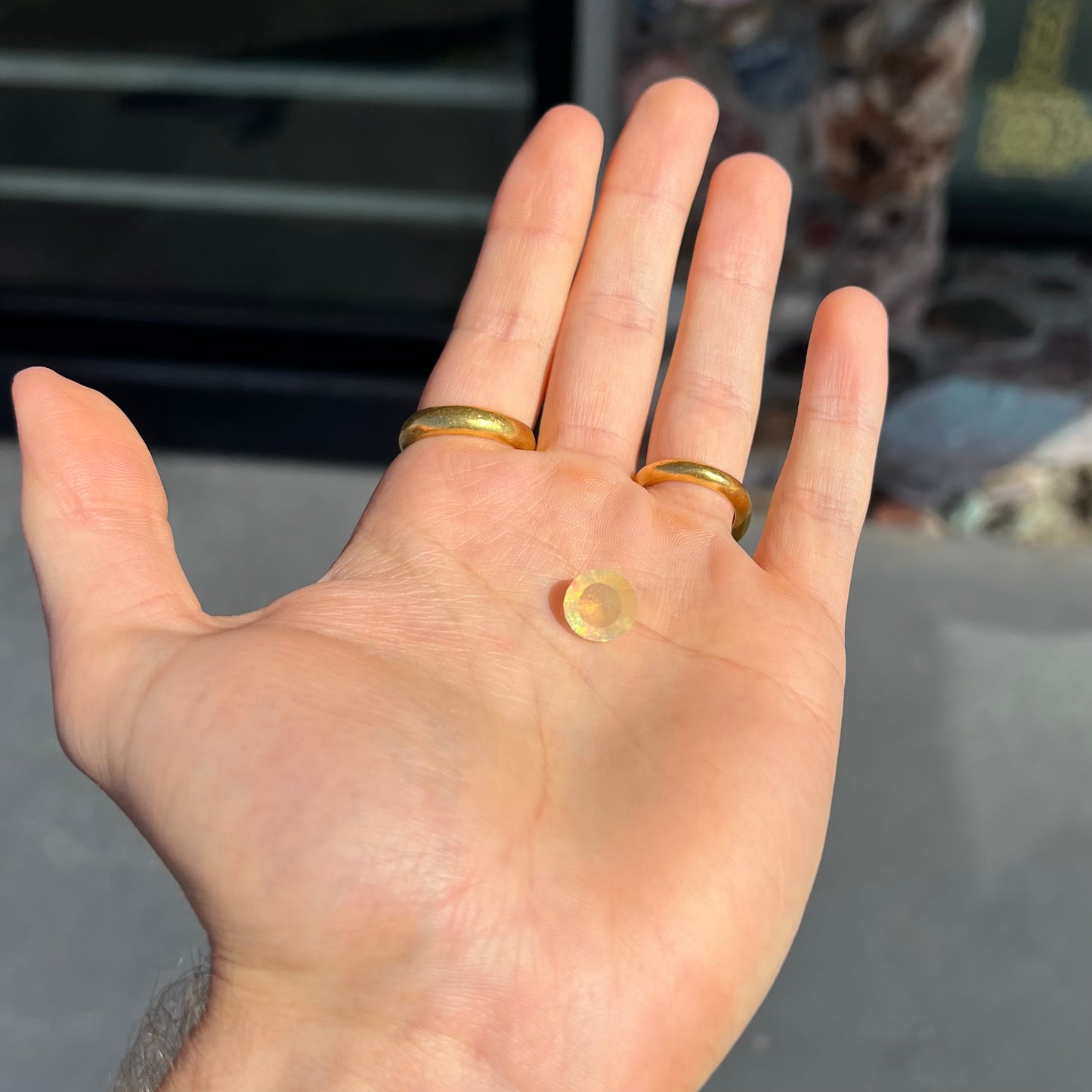 A loose, round faceted Mexican fire opal gemstone. The stone is transluscent light orange color with rainbow play of color in the sunlight.
