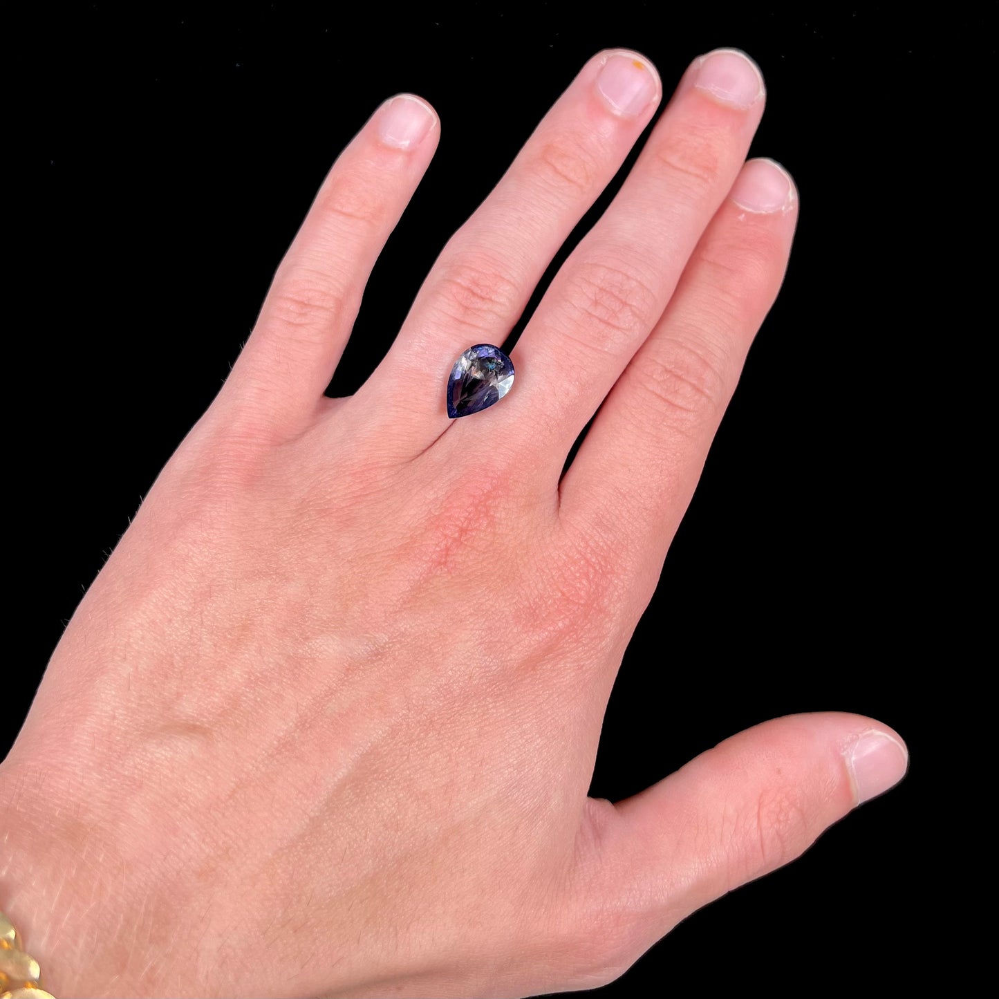A loose, pear shaped bicolor iolite gemstone. The stone shows violite purple and silver colors.