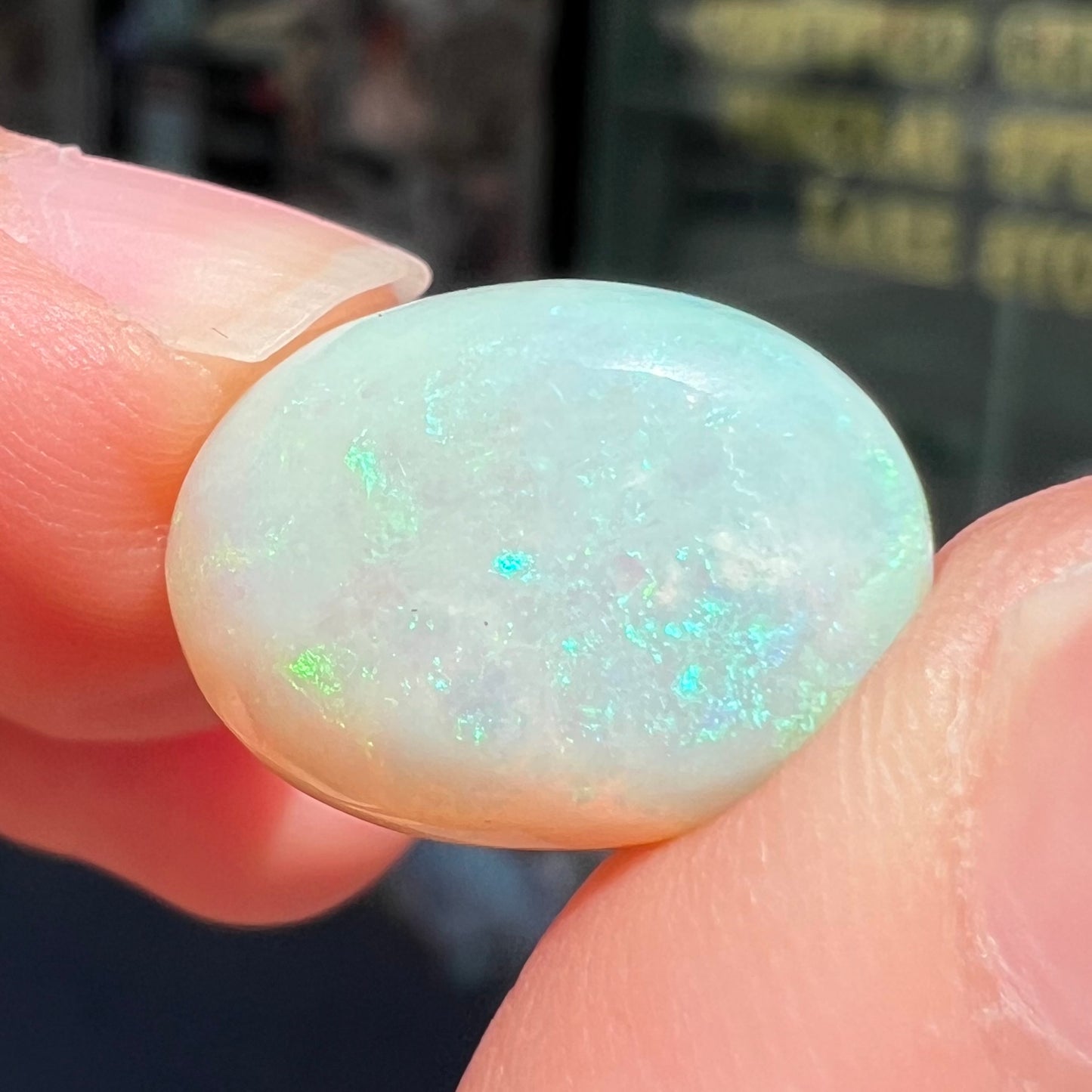 An oval cabochon cut white opal stone from Coober Pedy, Australia. The opal has subtle colors of green and blue.