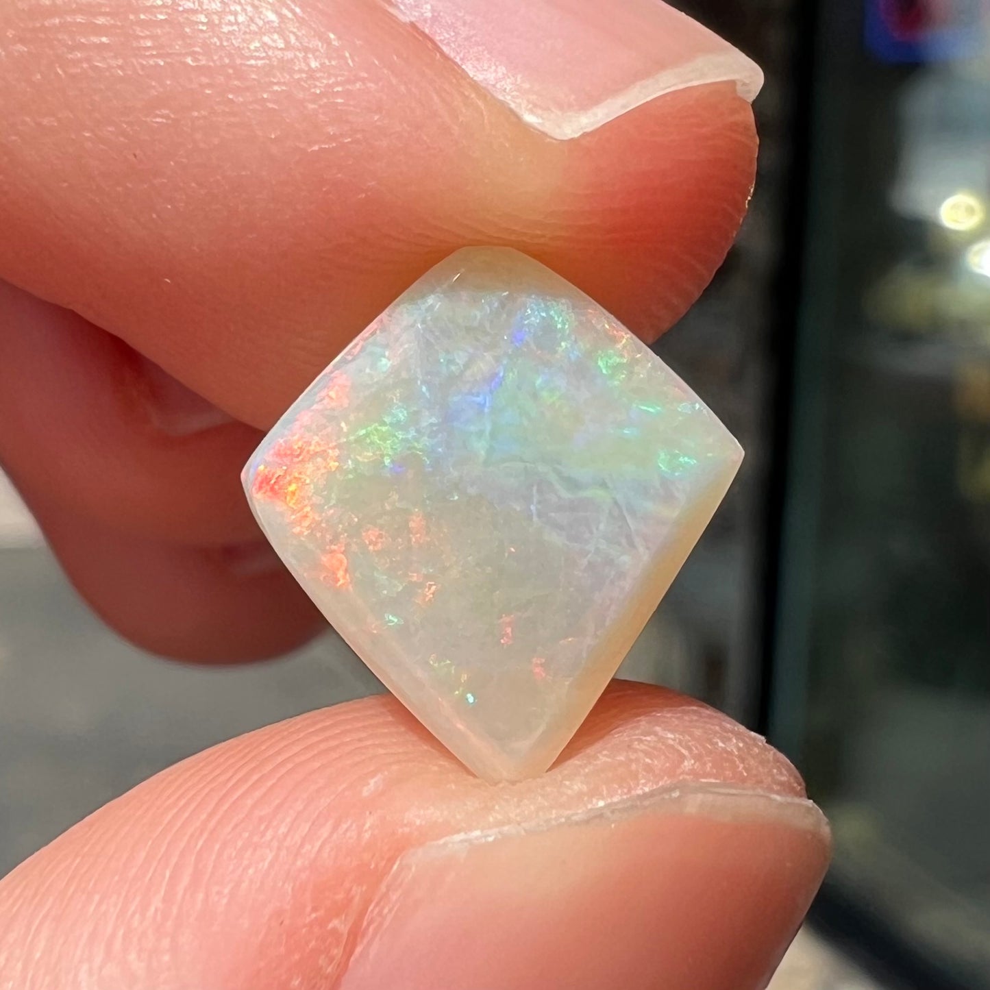 A loose, kite shaped white opal stone from Coober Pedy, Australia. The stone has subdued red colors.