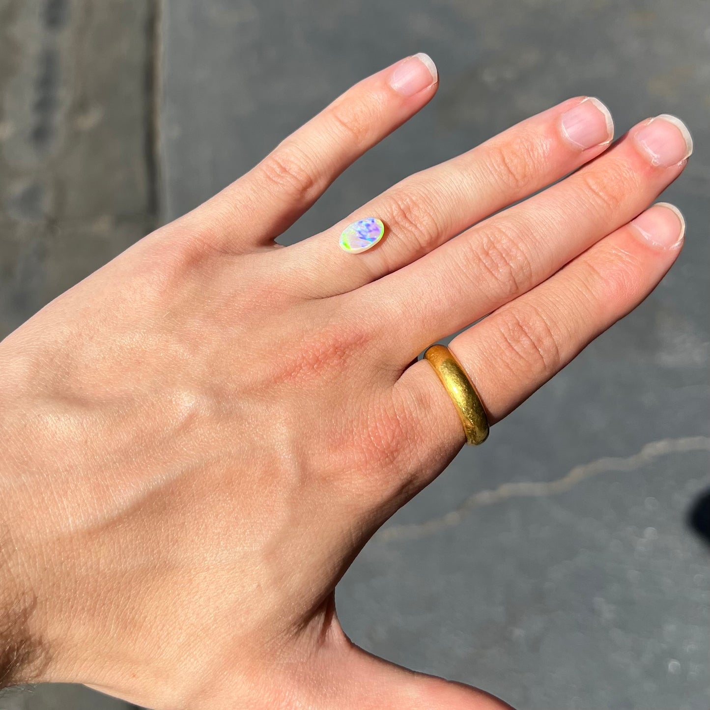 An oval cabochon cut white opal stone from Coober Pedy, Australia. The opal brilliantly shines green and orange colors.