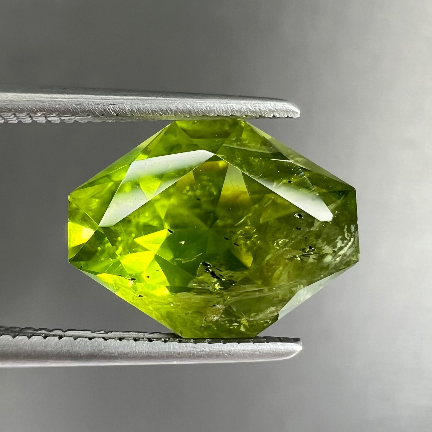 A loose, modified octagon peridot stone. The stone is a yellow green color.