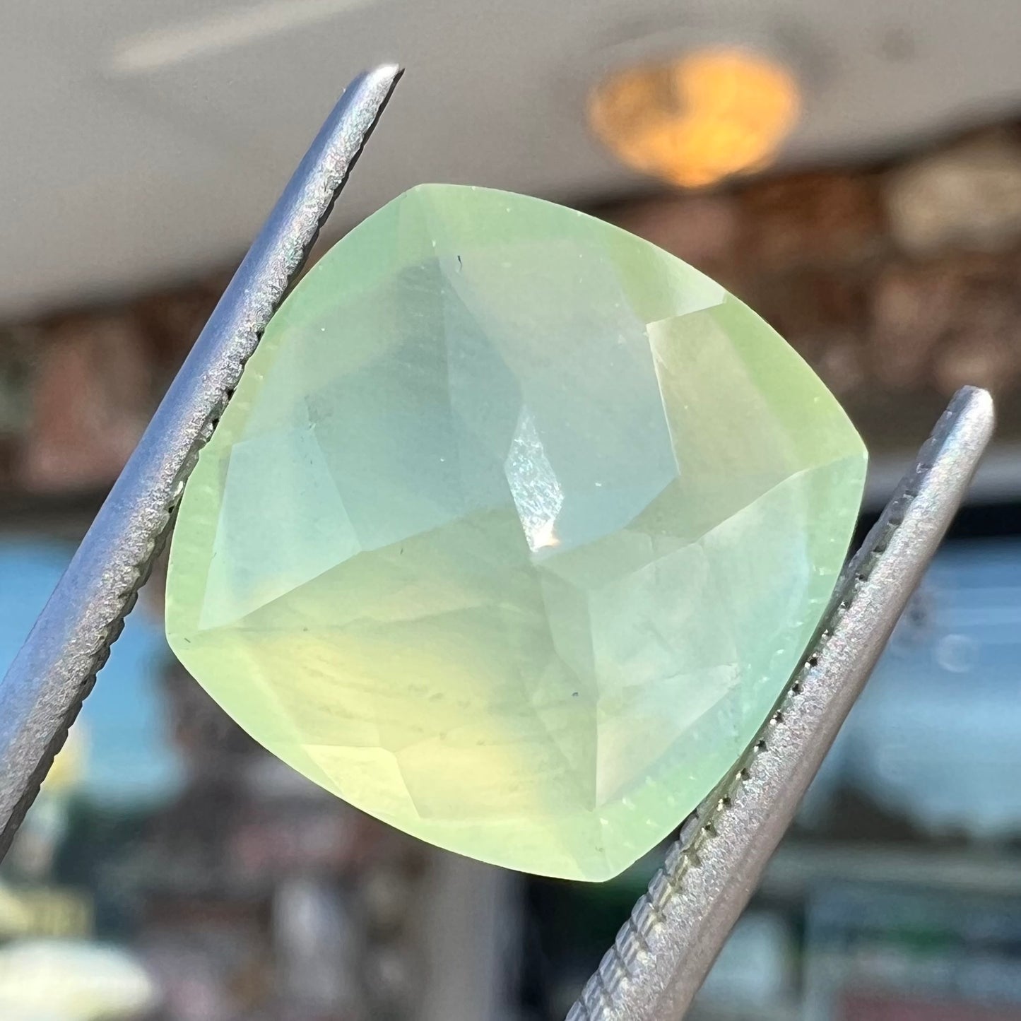 A loose, checkerboard cushion cut prehnite gemstone. The stone is a sleepy yellow green color.