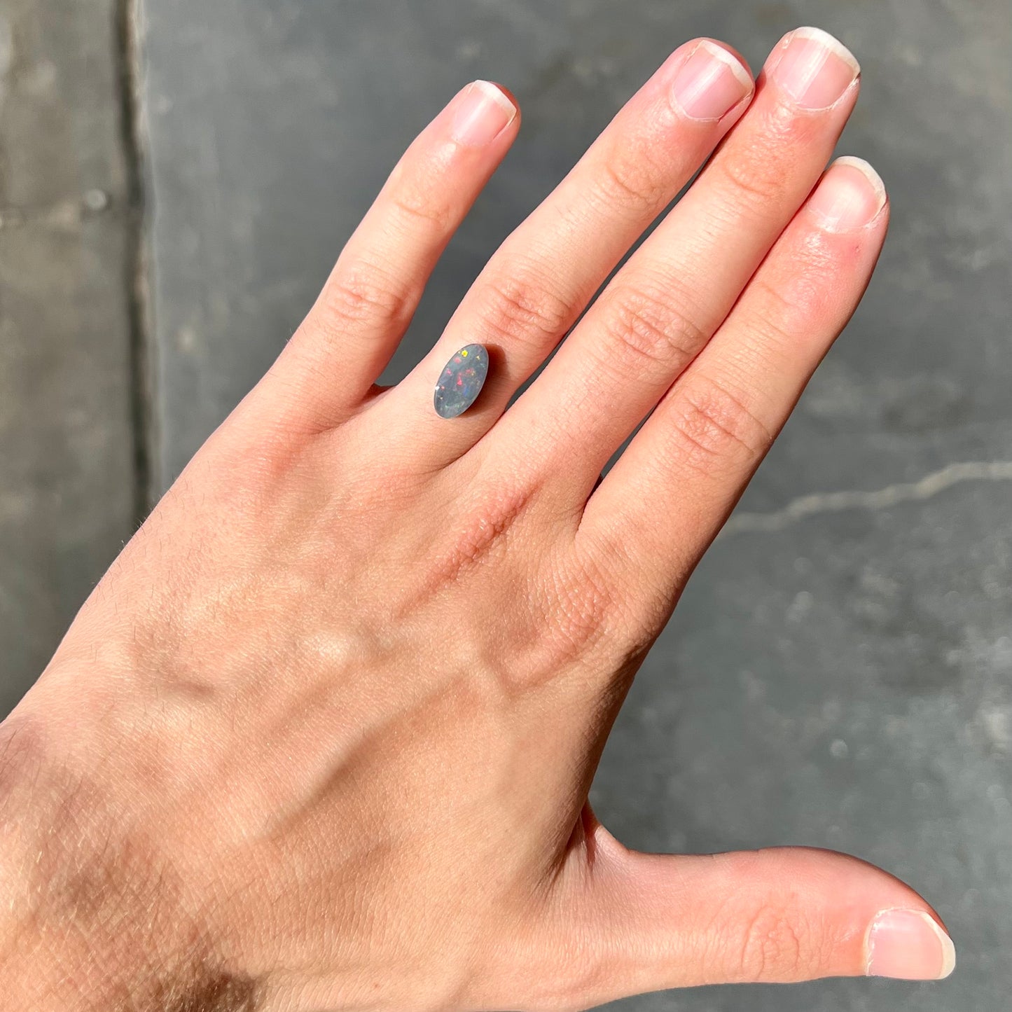 A loose, 3.01 carat, oval cut semi-black opal stone from Lightning Ridge, Australia. The opal has red colors.