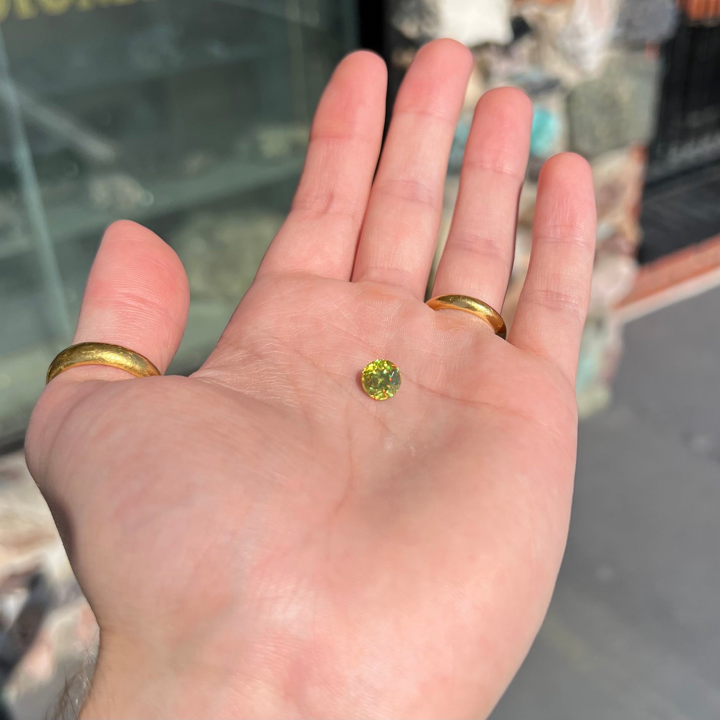 A loose, round brilliant cut sphene gemstone. The stone is green with orange, green, blue, and yellow flashes.