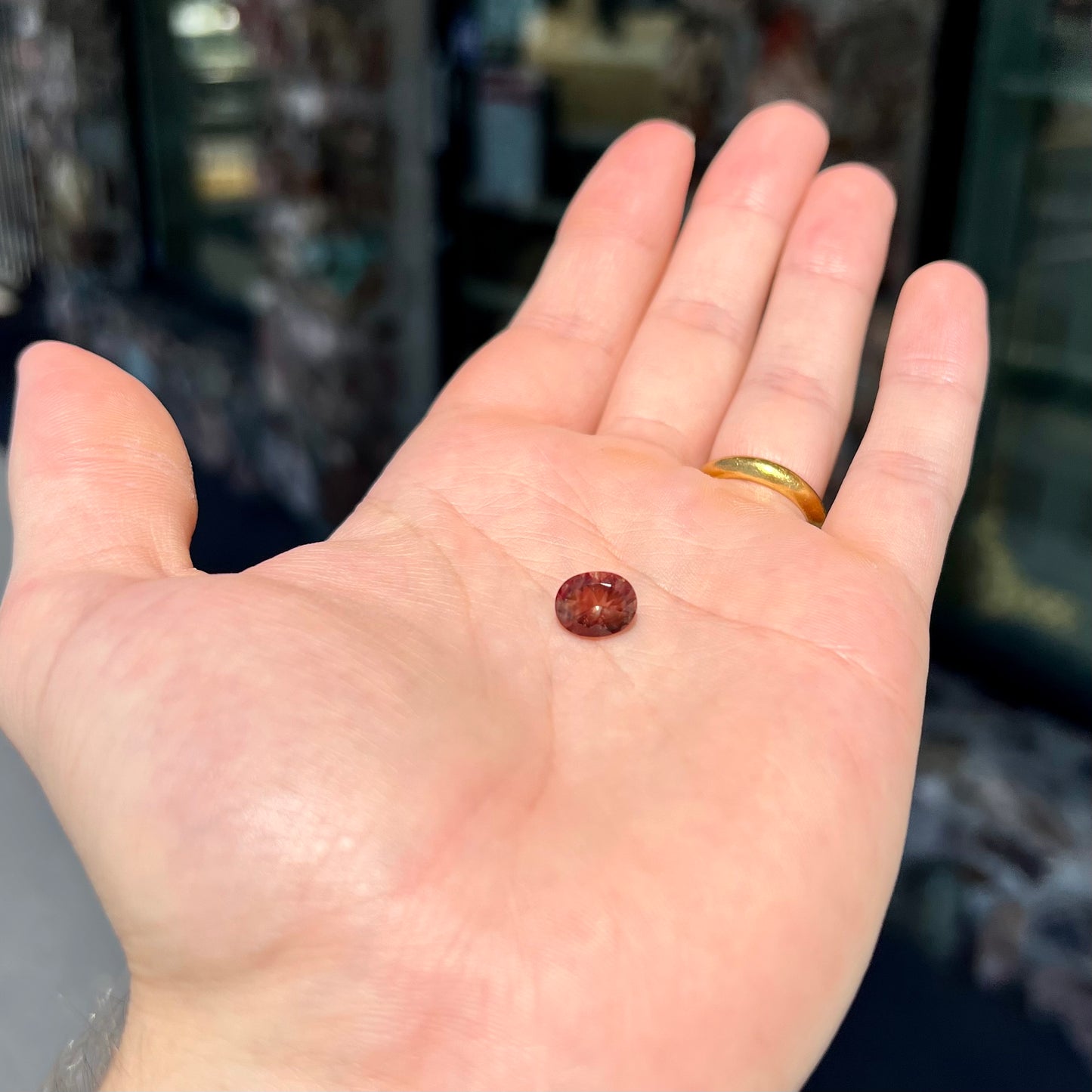 A loose, oval cut oregon sunstone.  The gem is reddish orange with a green secondary color.