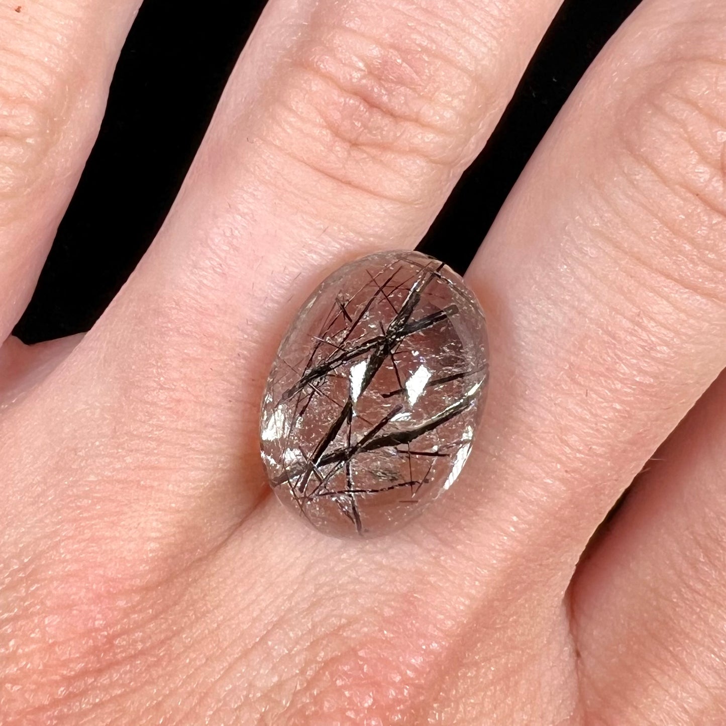 A loose, oval cabochon cut clear quartz stone with black tourmaline needle inclusions.