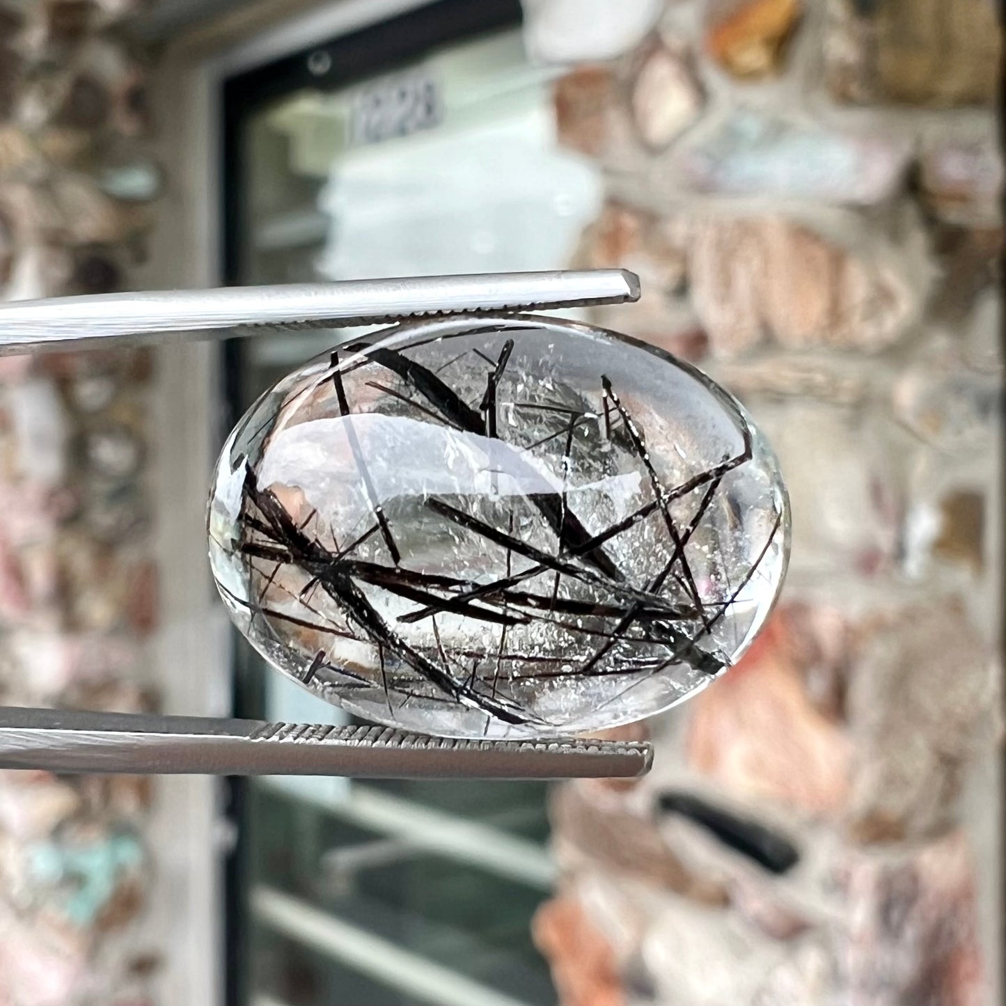 A loose, oval cabochon cut clear quartz stone with black tourmaline needle inclusions.