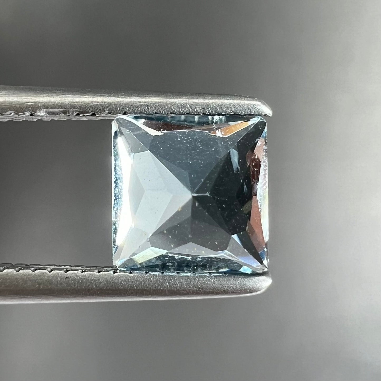 A loose, princess cut aquamarine gemstone. The stone is a light blue color.