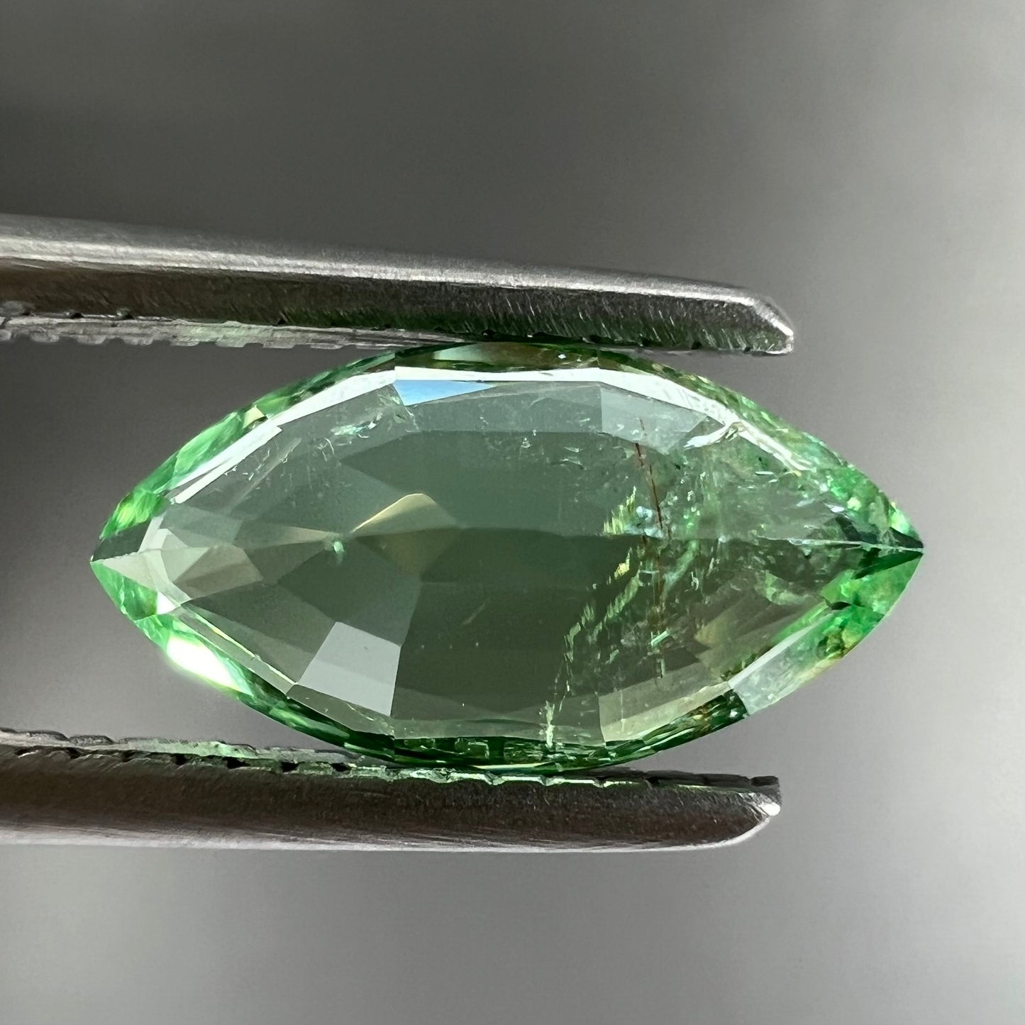 A faceted marquise cut electric green tourmaline gemstone. The stone has an eye-visible rutile needle inclusion.