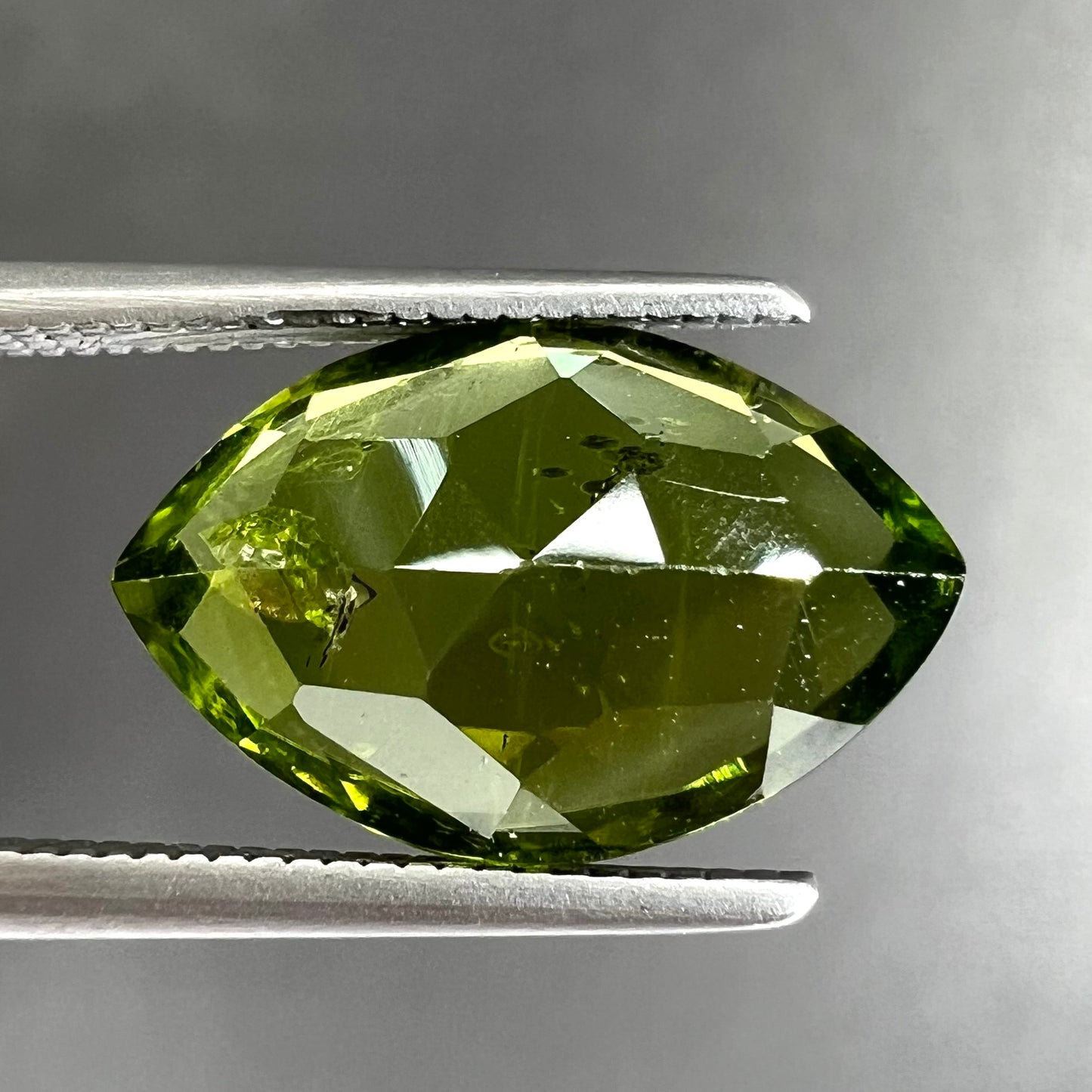 A loose, marquise cut peridot gemstone. The stone is an olive green color.