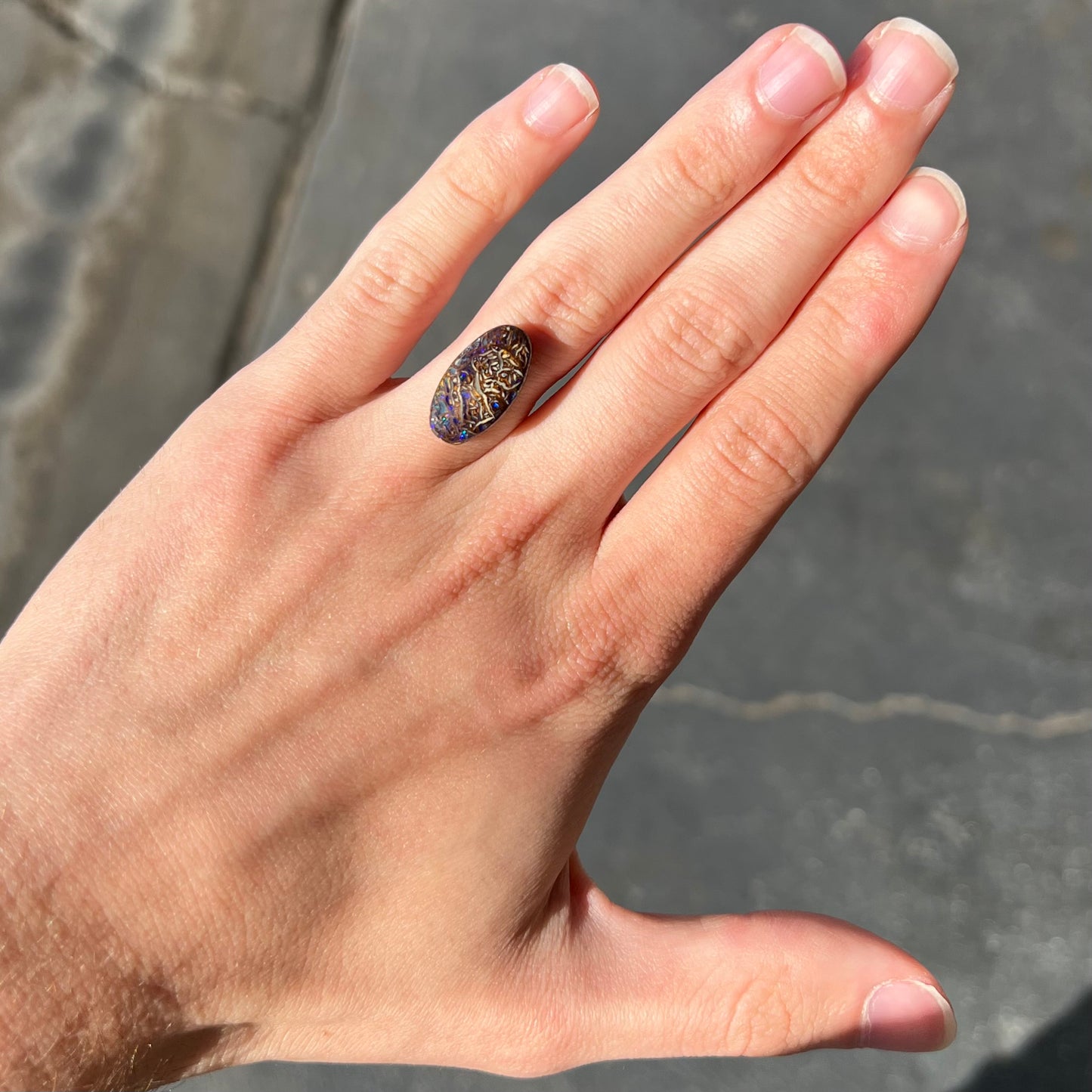 An oval cabochon cut Koroit boulder matrix opal stone. The opal has blue colors.