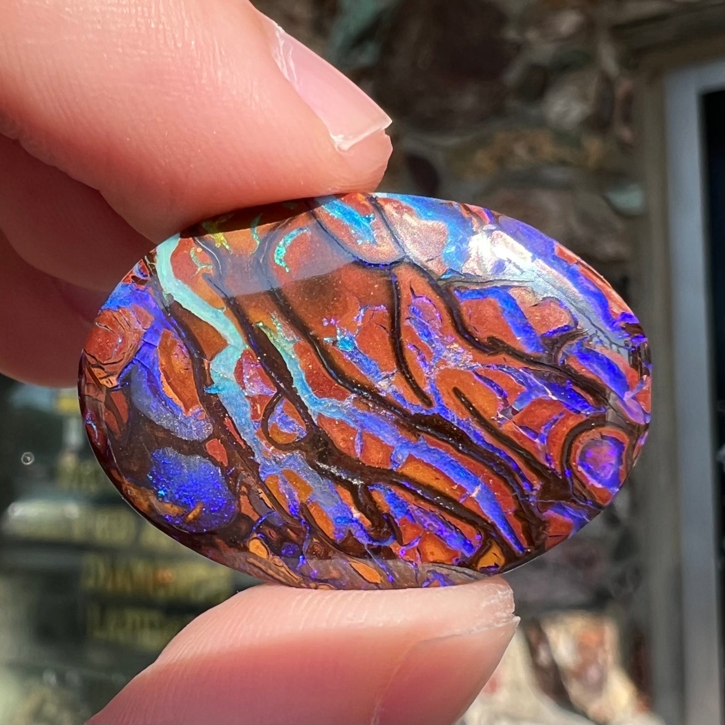A loose, oval cabochon cut boulder opal from Koroit, Australia. The opal has violet and purple veins.