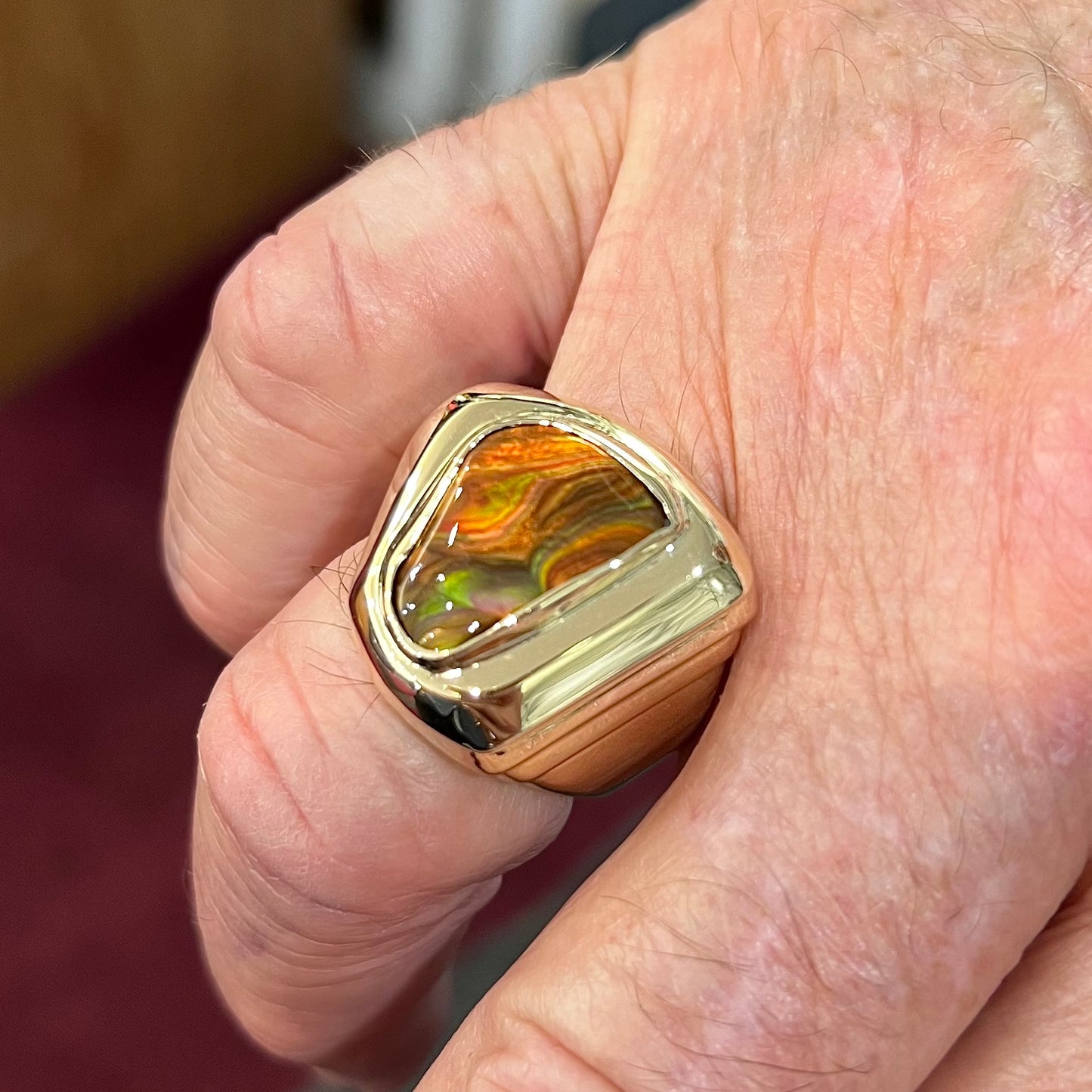 A heavy, yellow gold men's ring mounted with a Mexican fire agate stone. The fire agate has orange, green, red, and purple colors.
