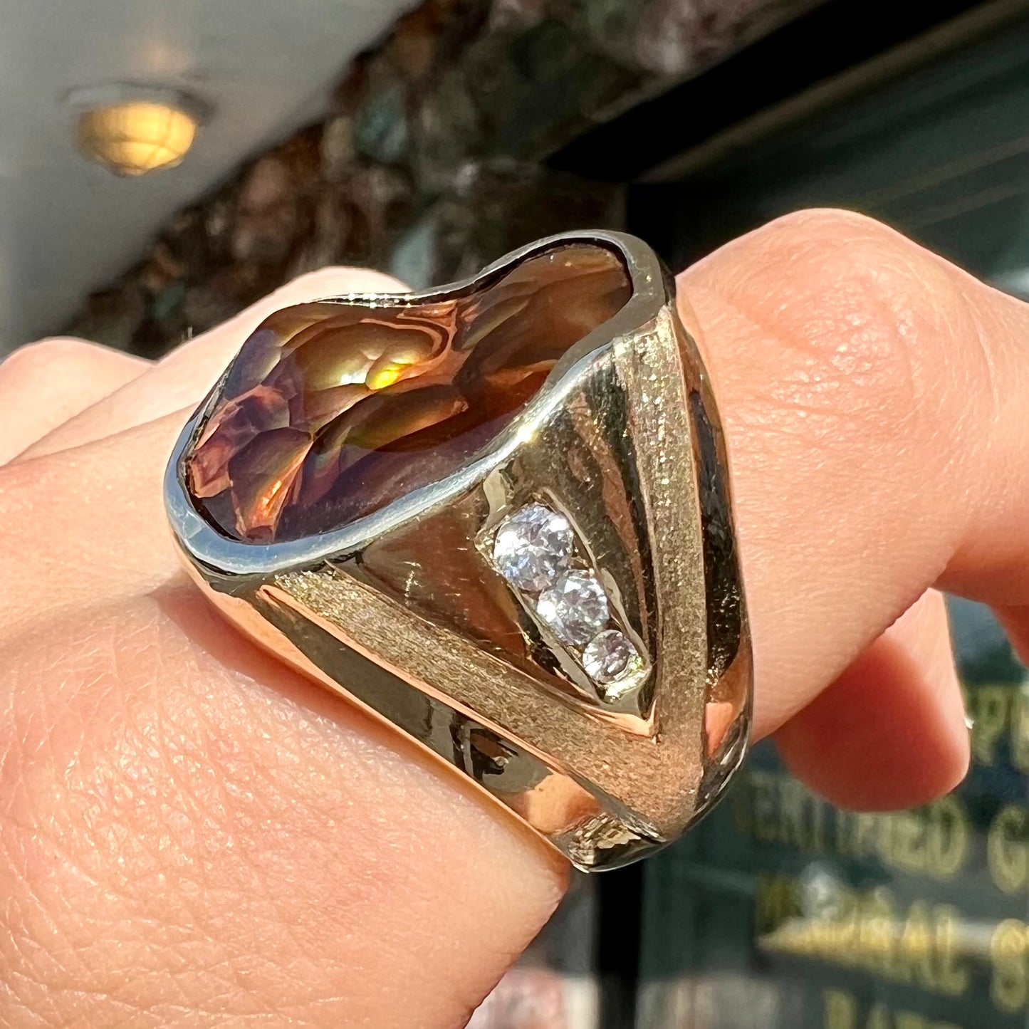 A men's heavy yellow gold ring set with a Mexican fire agate stone and three round brilliant cut diamond accents.