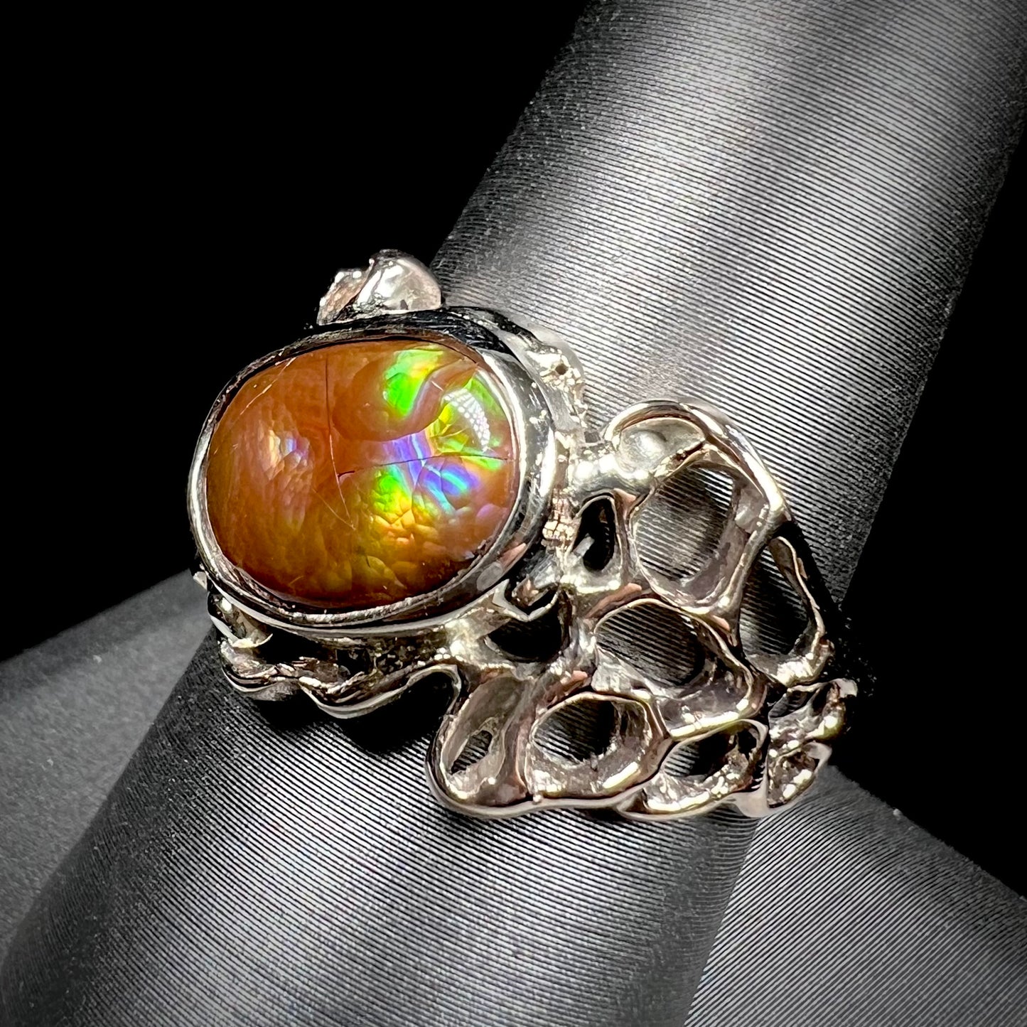 An organic-style white gold men's ring, bezel set with an oval cut Mexican fire agate stone.  The stone is green and purple.