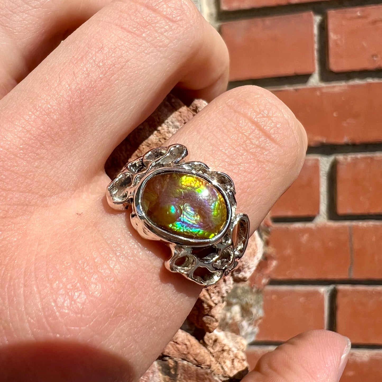 An organic-style white gold men's ring, bezel set with an oval cut Mexican fire agate stone.  The stone is green and purple.