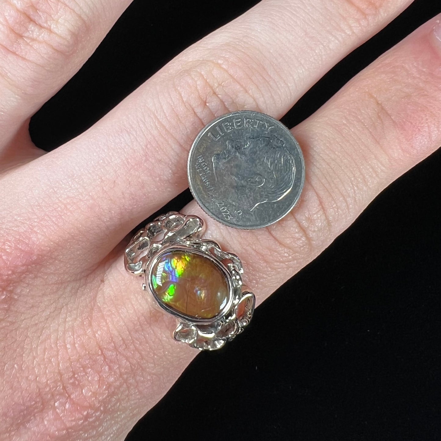 An organic-style white gold men's ring, bezel set with an oval cut Mexican fire agate stone.  The stone is green and purple.