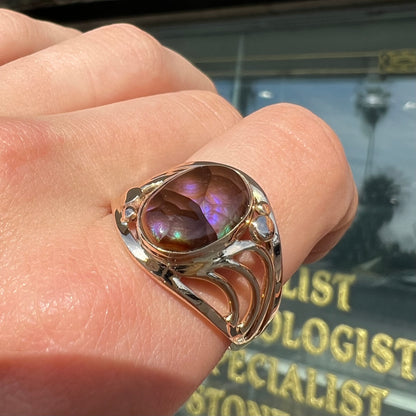 An oval cabochon cut fire agate with purple and blue colors set in a yellow gold men's ring.