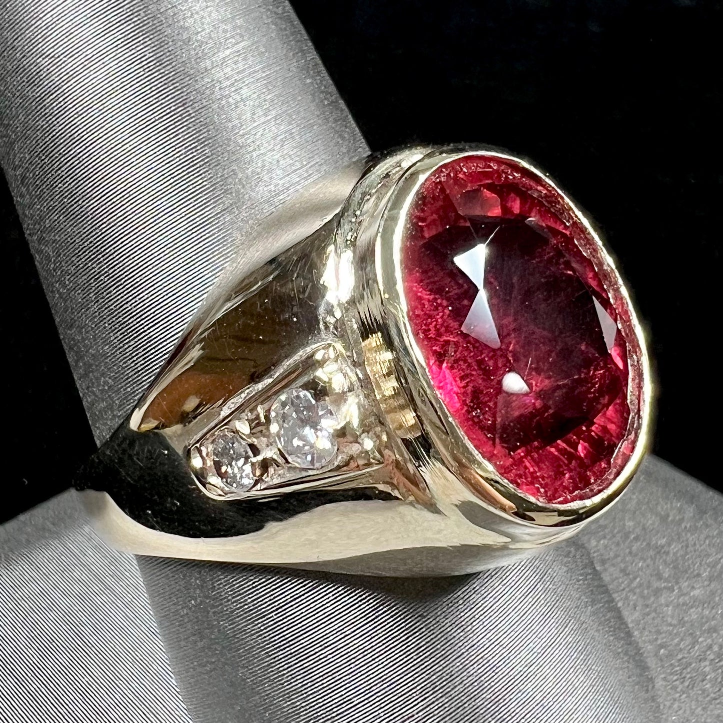 A men's yellow gold ring set with an oval cut rubellite tourmaline with diamond accents.