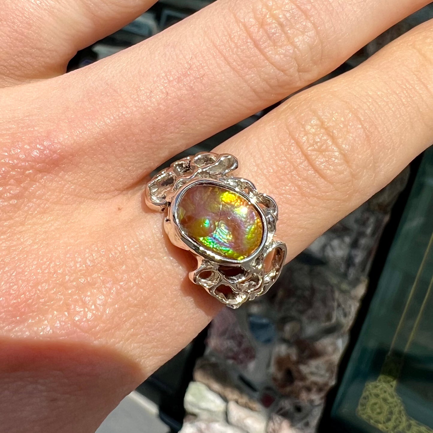 An organic-style white gold men's ring, bezel set with an oval cut Mexican fire agate stone.  The stone is green and purple.