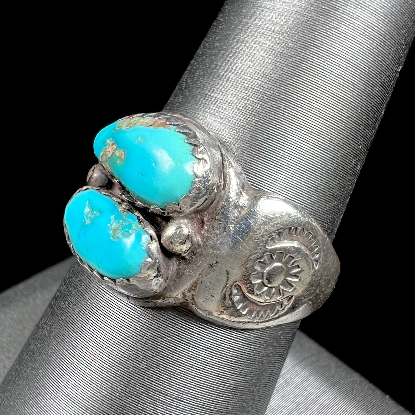 A unisex sterling silver ring bezel set with two Pilot Mountain turquoise stones.  The ring is stamped with sun patterns.