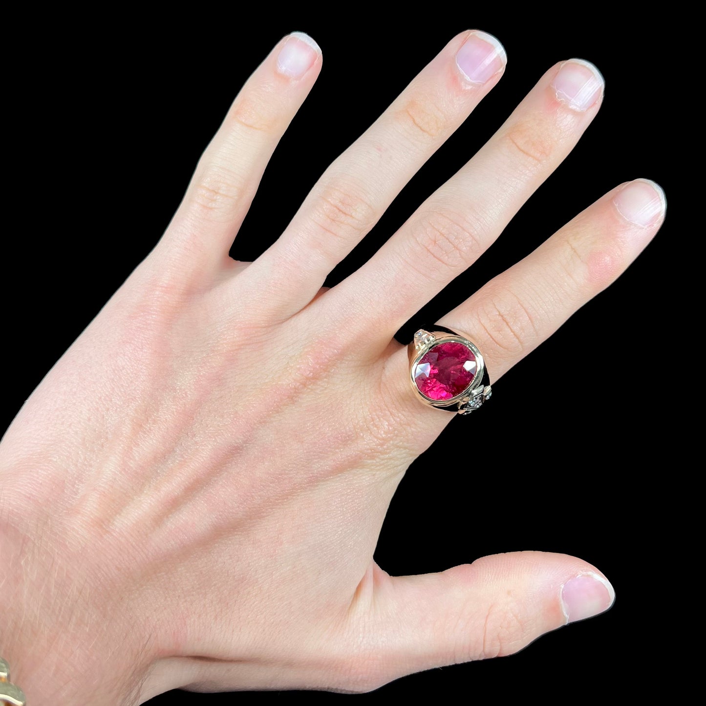 A men's yellow gold ring set with an oval cut rubellite tourmaline with diamond accents.