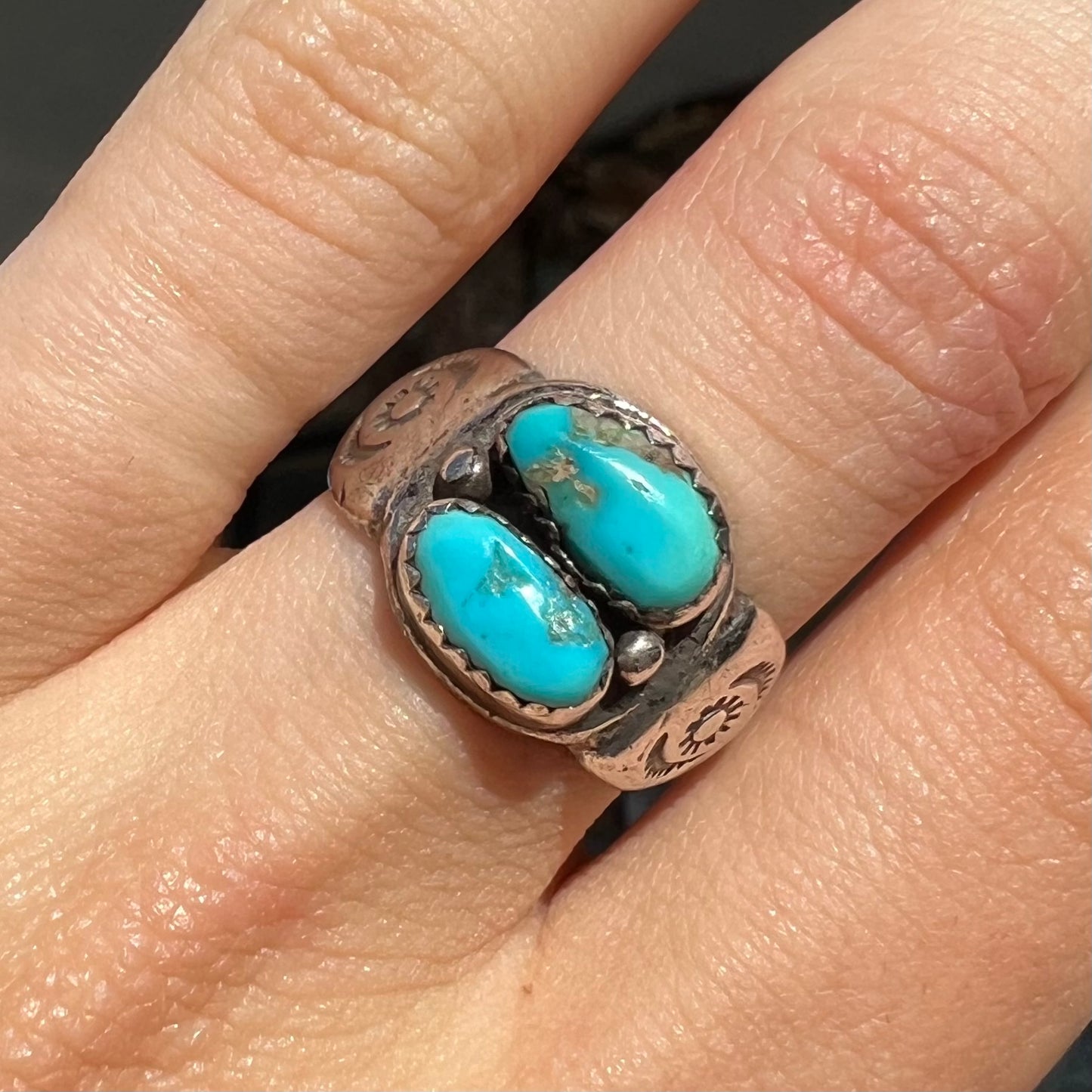 A unisex sterling silver ring bezel set with two Pilot Mountain turquoise stones.  The ring is stamped with sun patterns.