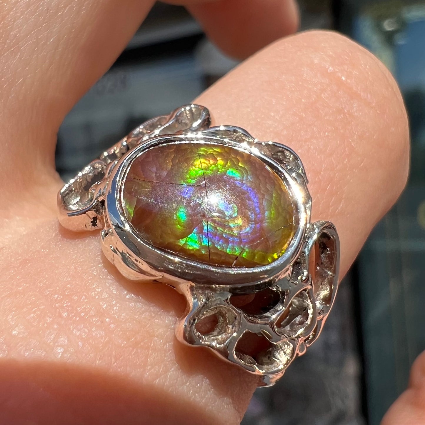 An organic-style white gold men's ring, bezel set with an oval cut Mexican fire agate stone.  The stone is green and purple.