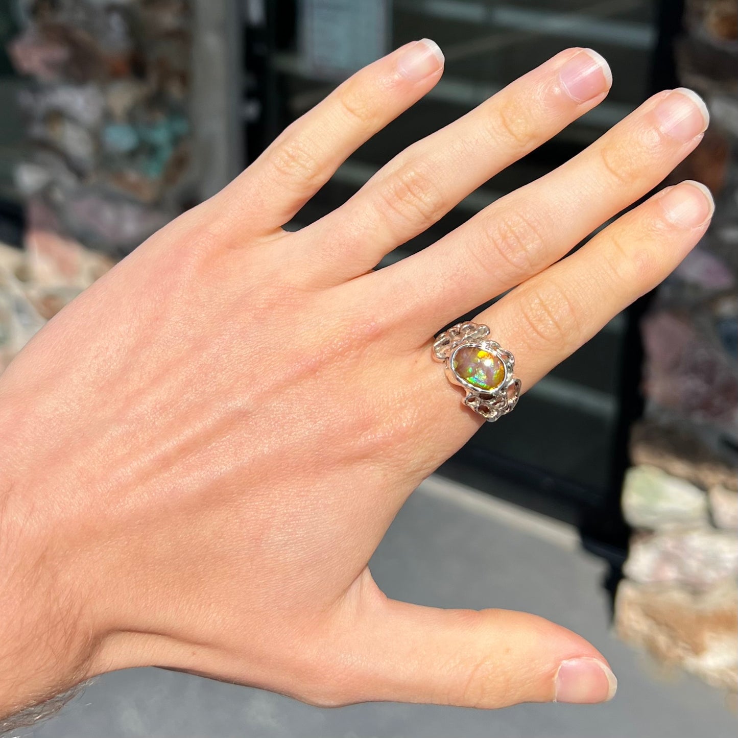 An organic-style white gold men's ring, bezel set with an oval cut Mexican fire agate stone.  The stone is green and purple.