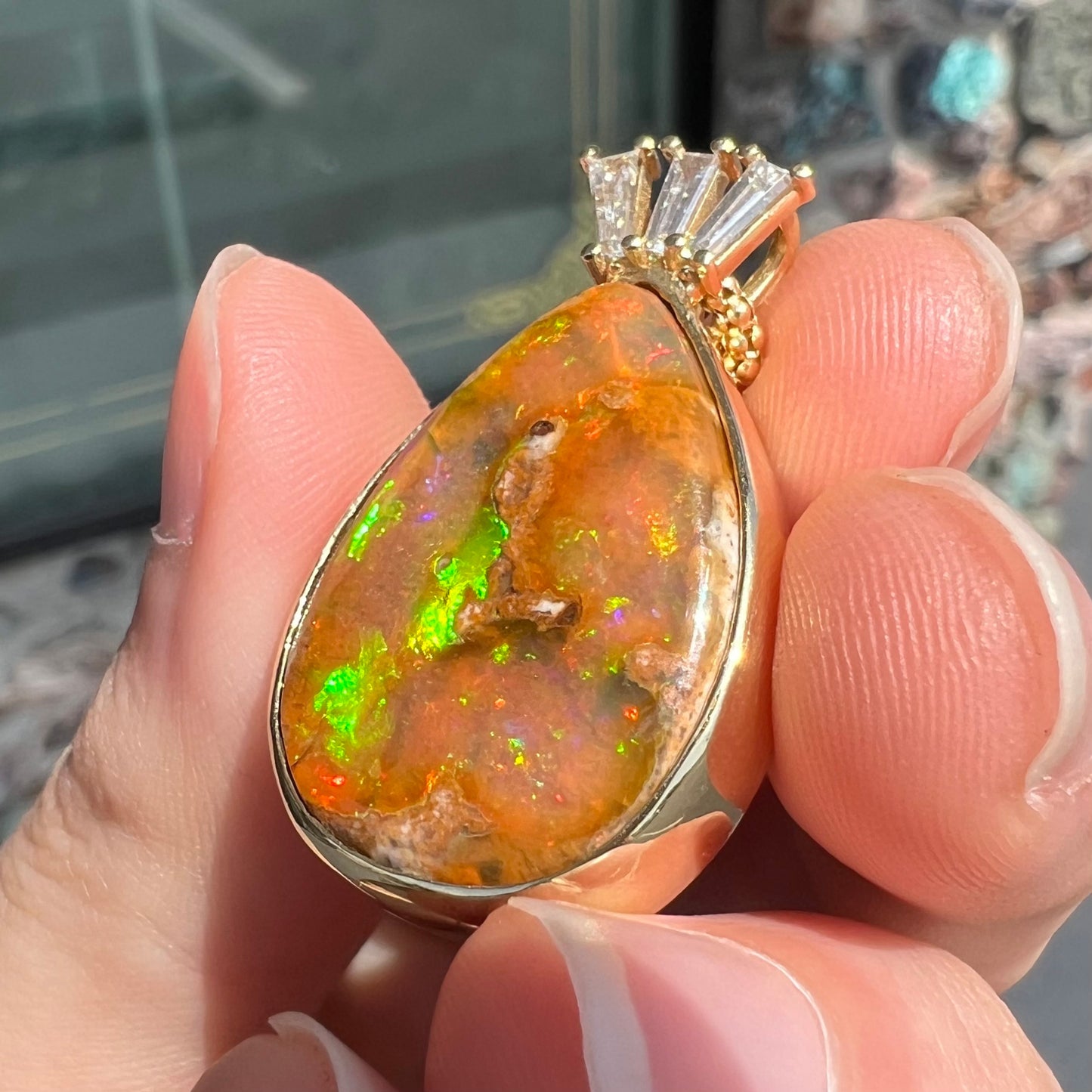 A unisex pear shaped fire opal pendant set with tapered baguette cut diamond accents in 18 karat gold.