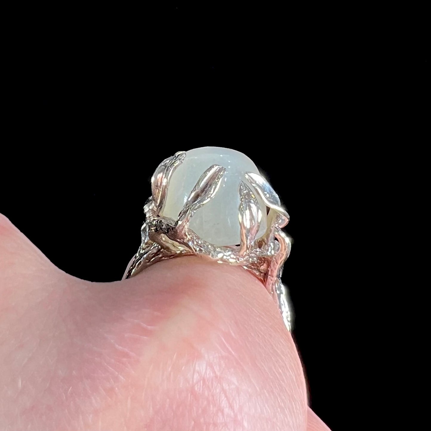 A ladies' organic style white gold moonstone ring. The moonstone shows white adularescence on a creamy white body color. Prongs resemble leaves holding the stone.