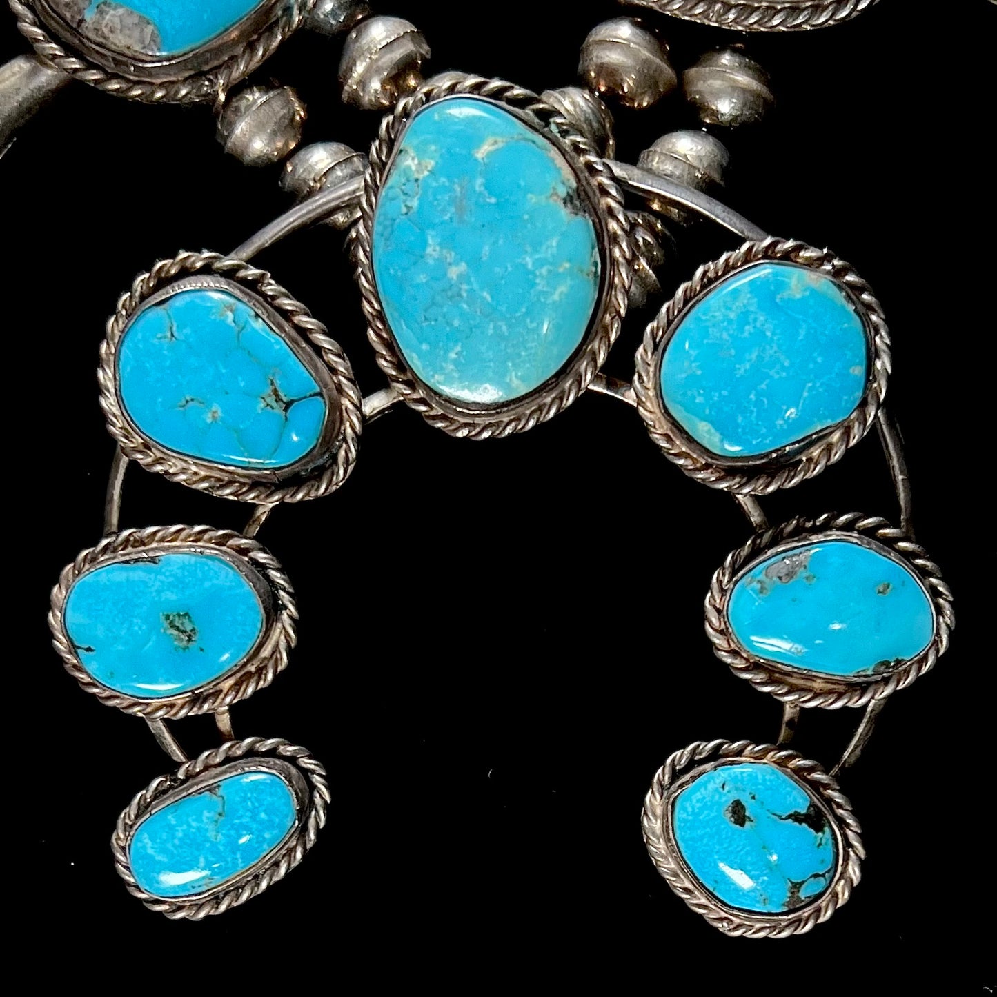 A sterling silver, Navajo style squash blossom necklace set with Morenci turquoise stones. The legnth is designed for women and children.