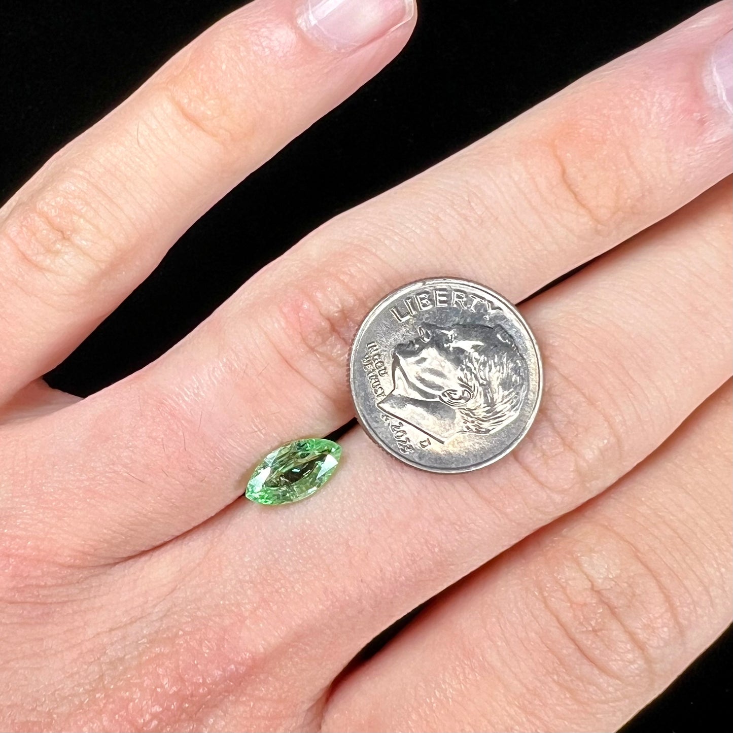 A faceted marquise cut electric green tourmaline gemstone. The stone has an eye-visible rutile needle inclusion.